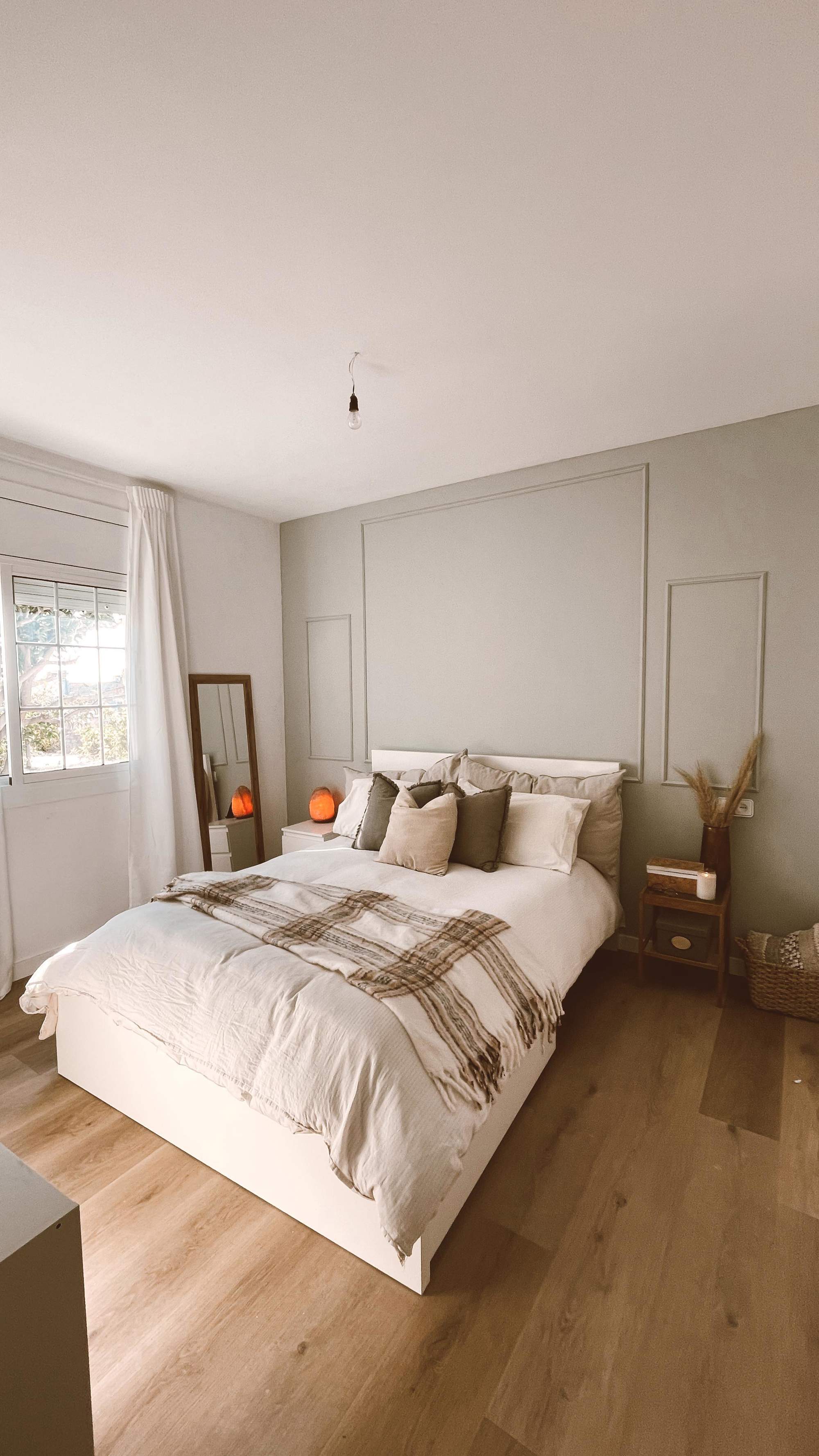 Dormitorio principal con cabecero verde original, cama con textiles otoñales y plaid de cuadros, y pavimento de madera.