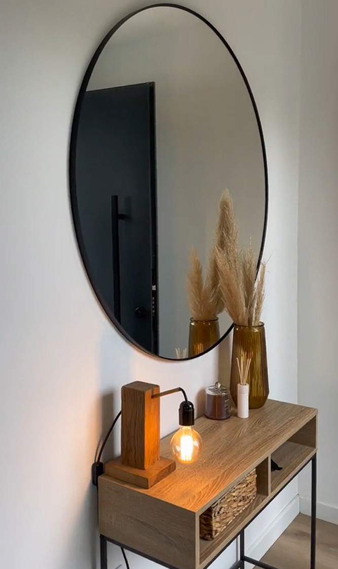 Recibidor con consola de madera, accesorios decorativos, lámpara de mesa y espejo redondo. 
