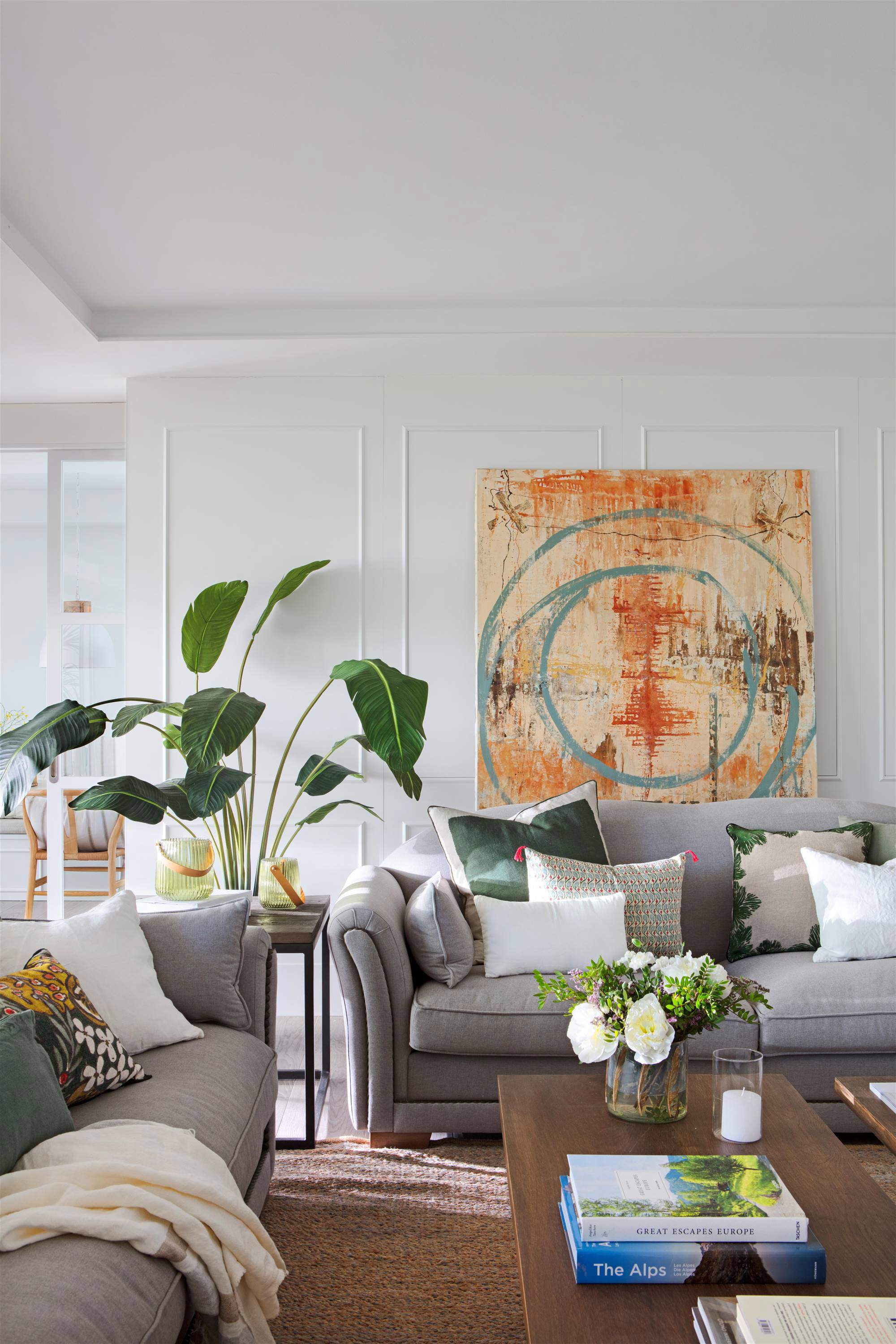 Salón con sofás grises, planta alta, molduras en paredes y cuadro. 