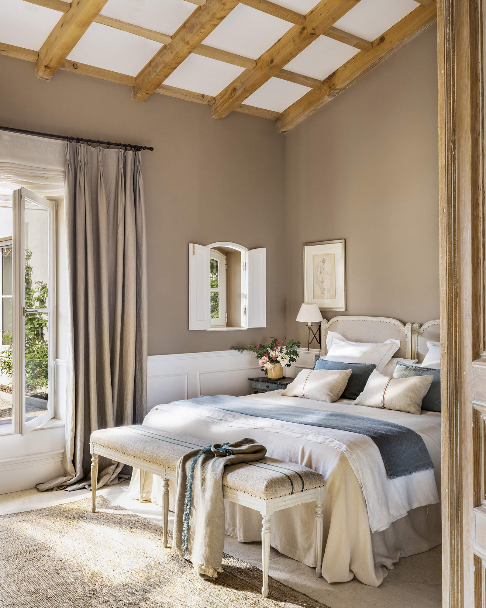 Dormitorio con vigas de madera, cabecero restaurado, cortinas de lino y arrimaderos blancos