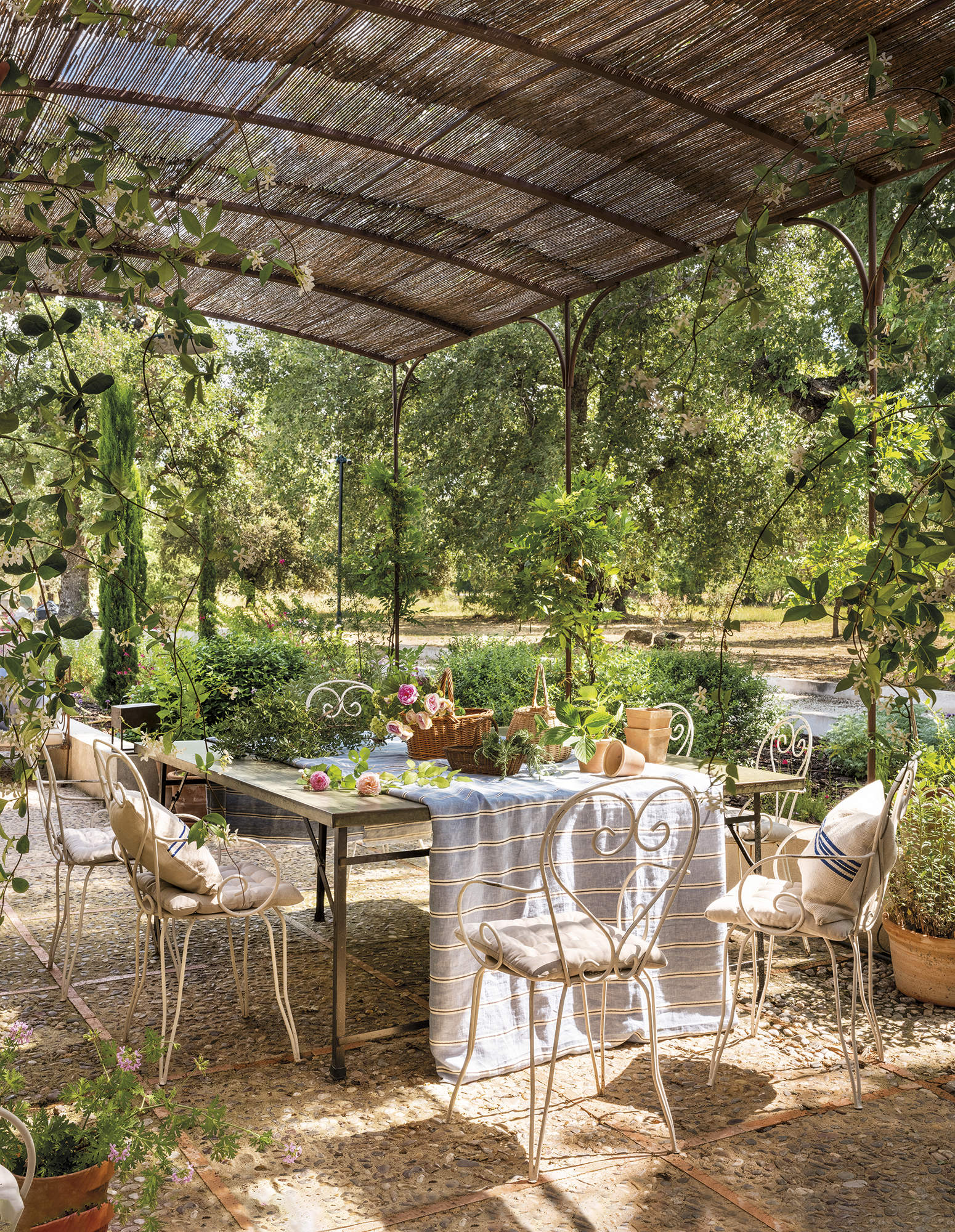 Comedor exterior con pérgola de hierro y cañizo, mesa y sillas de jardín