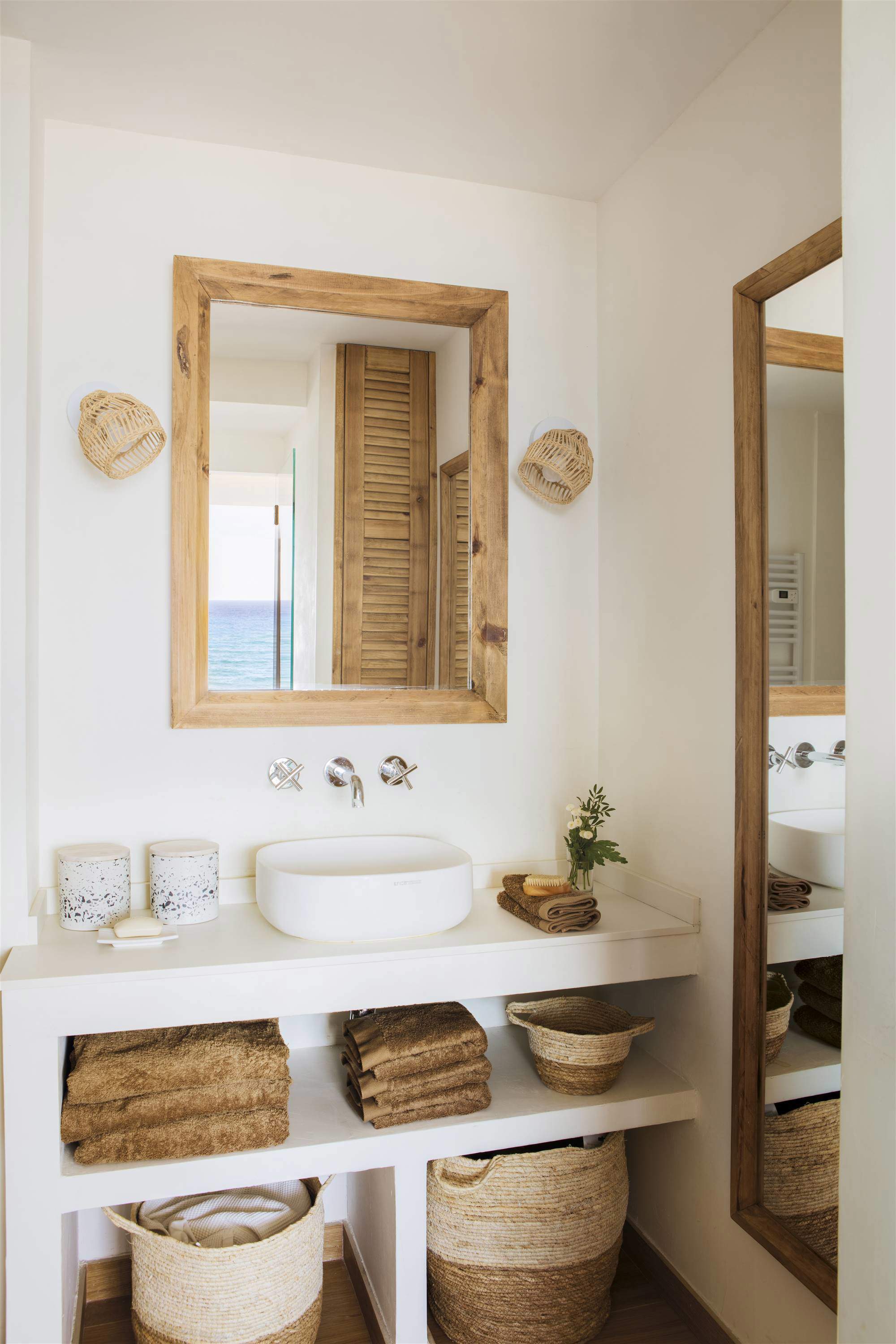 Baño con mueble bajolababo de obra, lavabo exento, espejo de madera, apliques de fibra y toallas marrones.