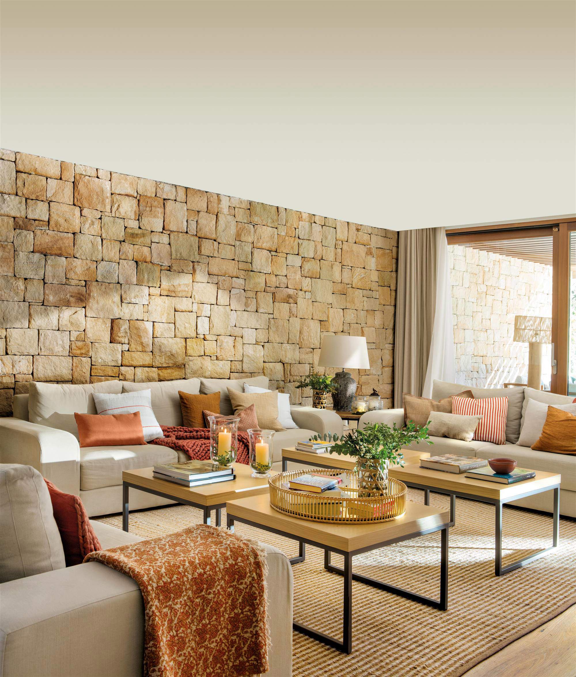 Salón neutro con pared de piedra, mesas de centro, sofás y alfombra.