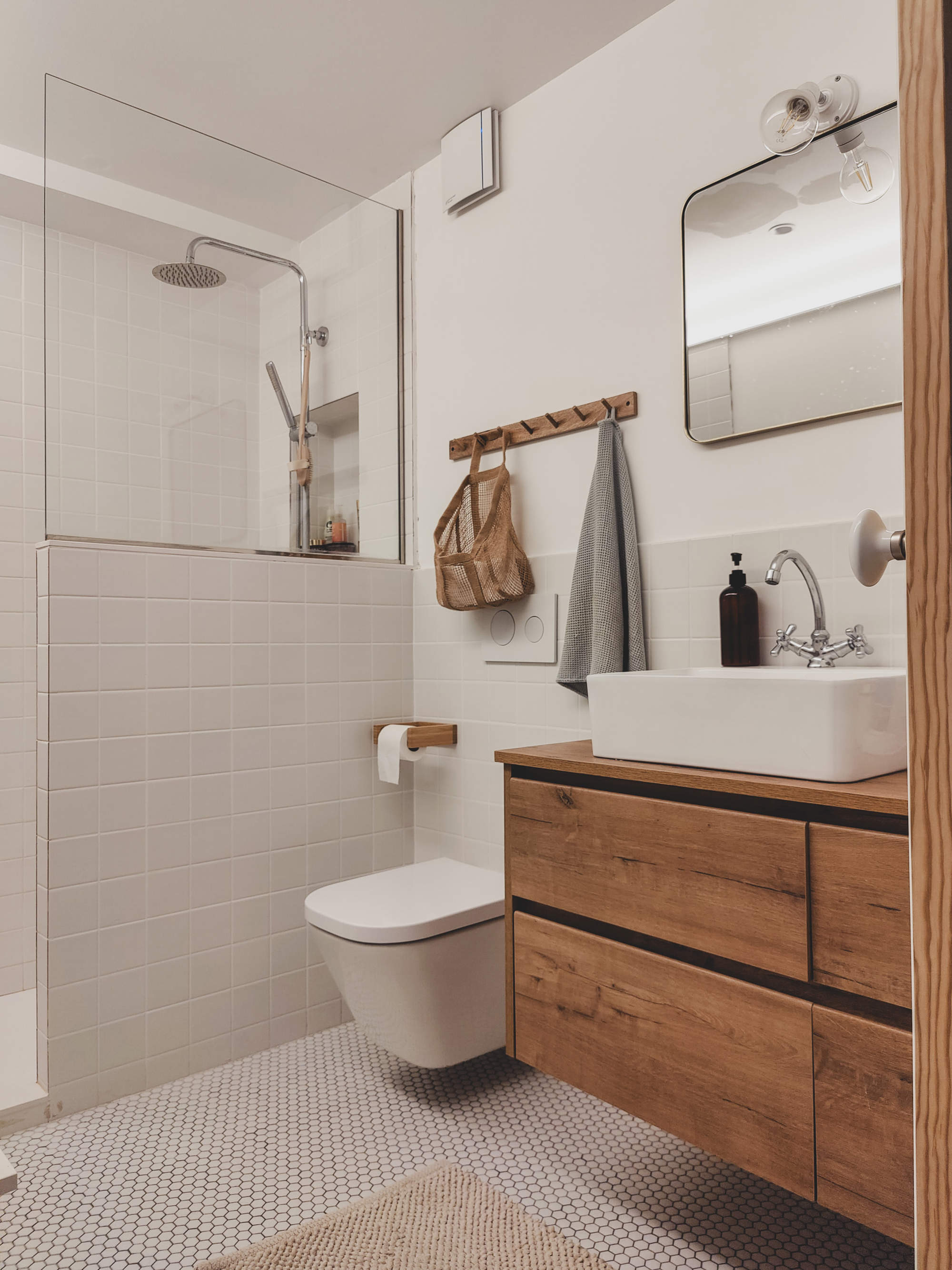 Baño con mueble bajolavabo volado de madera, azulejos a cuadros en el pavimento, ducha con mampara y murete.
