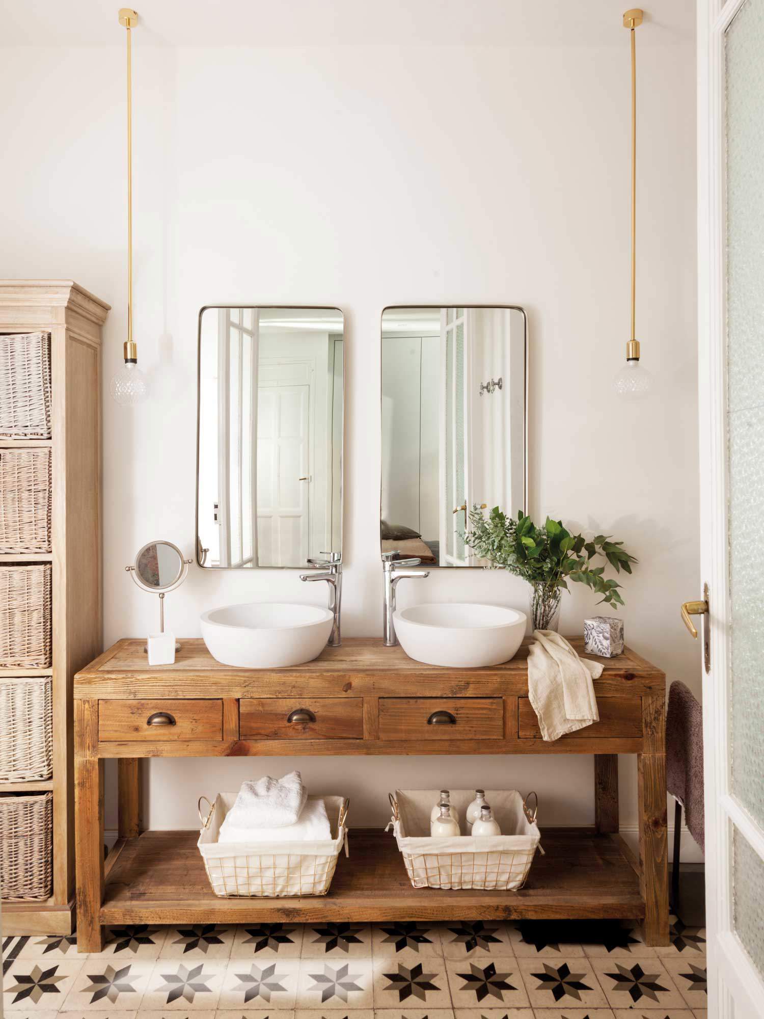 Baño con consola de madera a modo de mueble bajolavabo, lavamanos exentos redondos, espejos, lámparas suspendidas y suelo hidraúlico