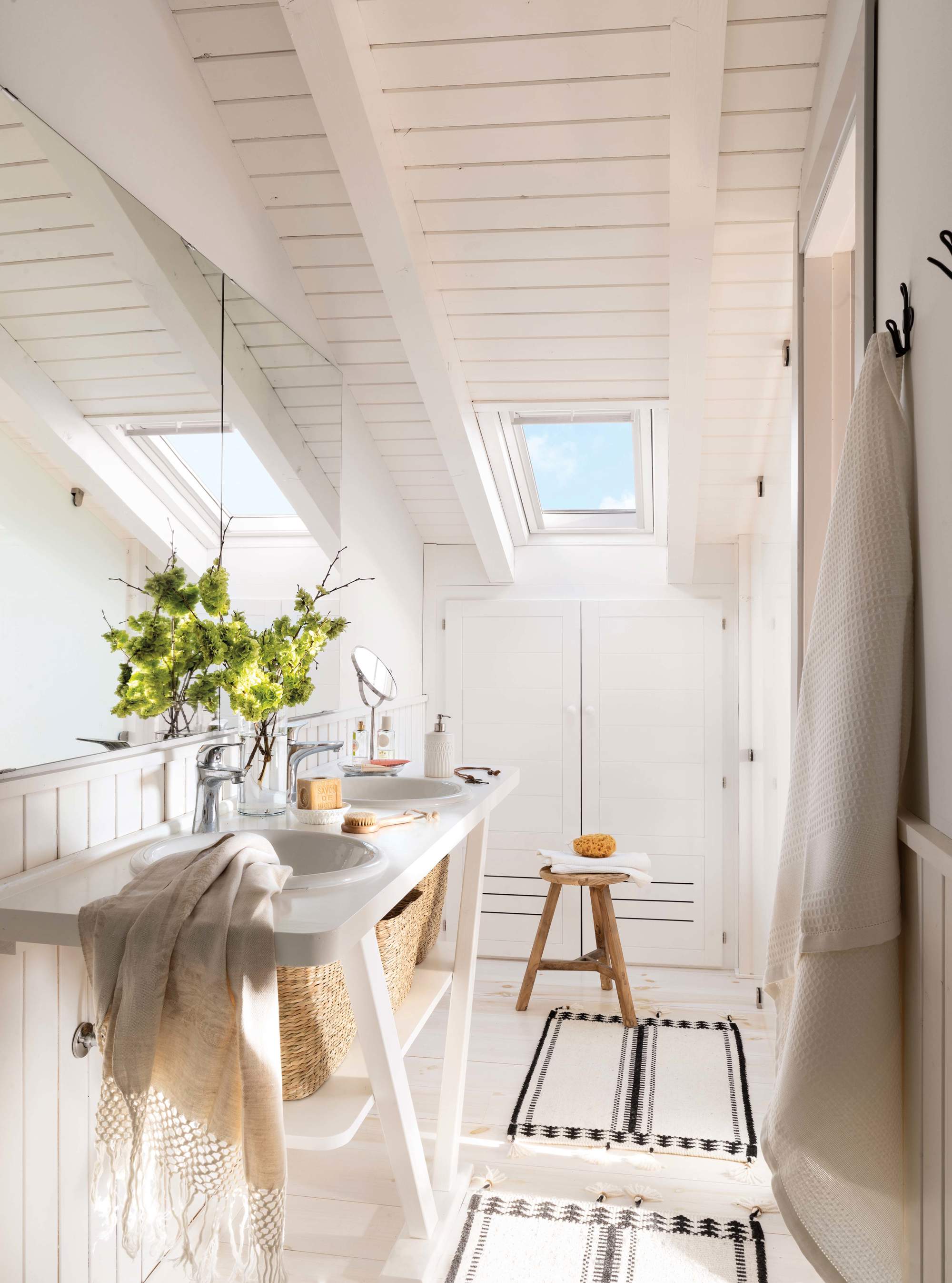 Baño con mueble abierto de lavabo lacado en blanco, alfombras, toallas y taburete