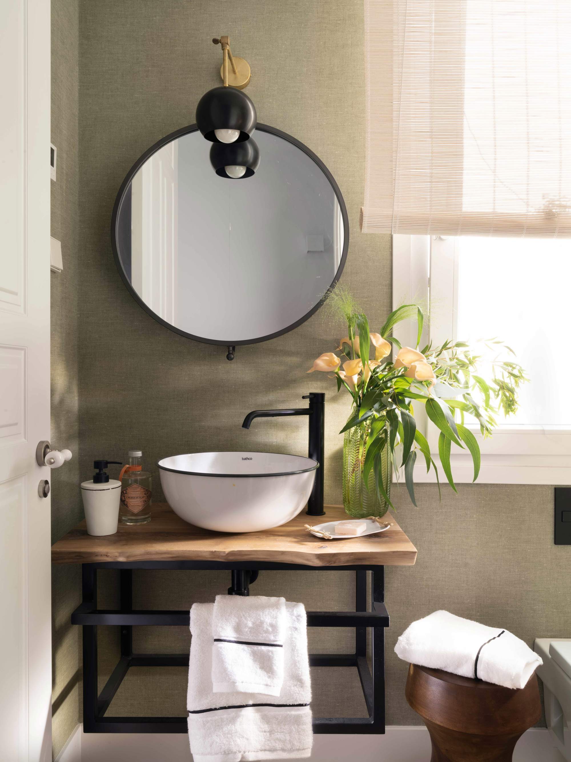 Baño con mueble de lavabo volado en madera y metal, espejo, aplique, lavamanos exento, grifería negra y flores