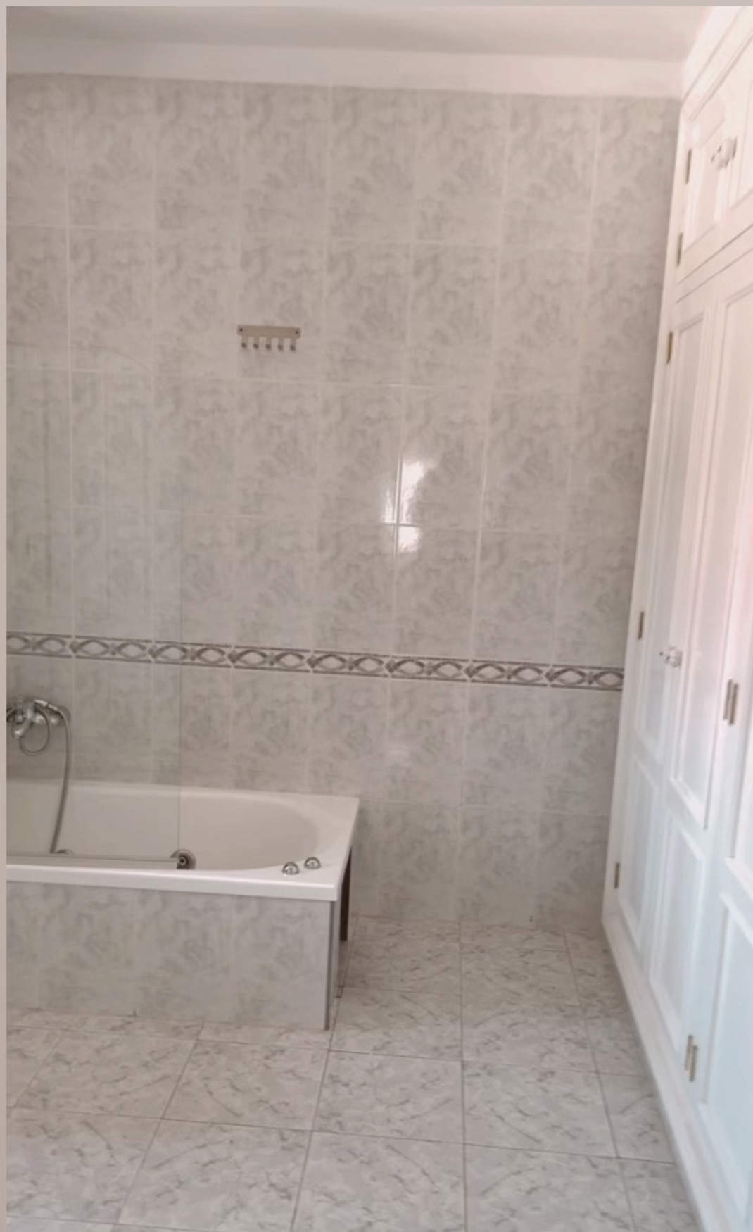 Un cuarto de baño con bañera, armarios y azulejos y baldosas antiguas.