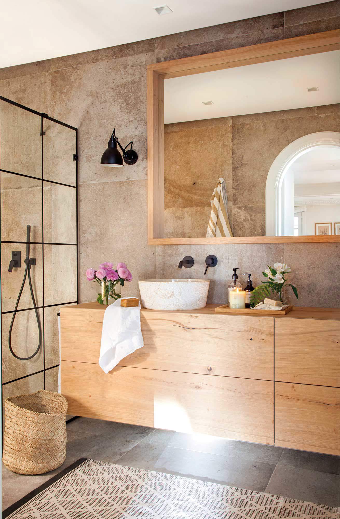 Baño con mueble de madera clara, mampara acristalada, espejo, aplique negro y alfombra