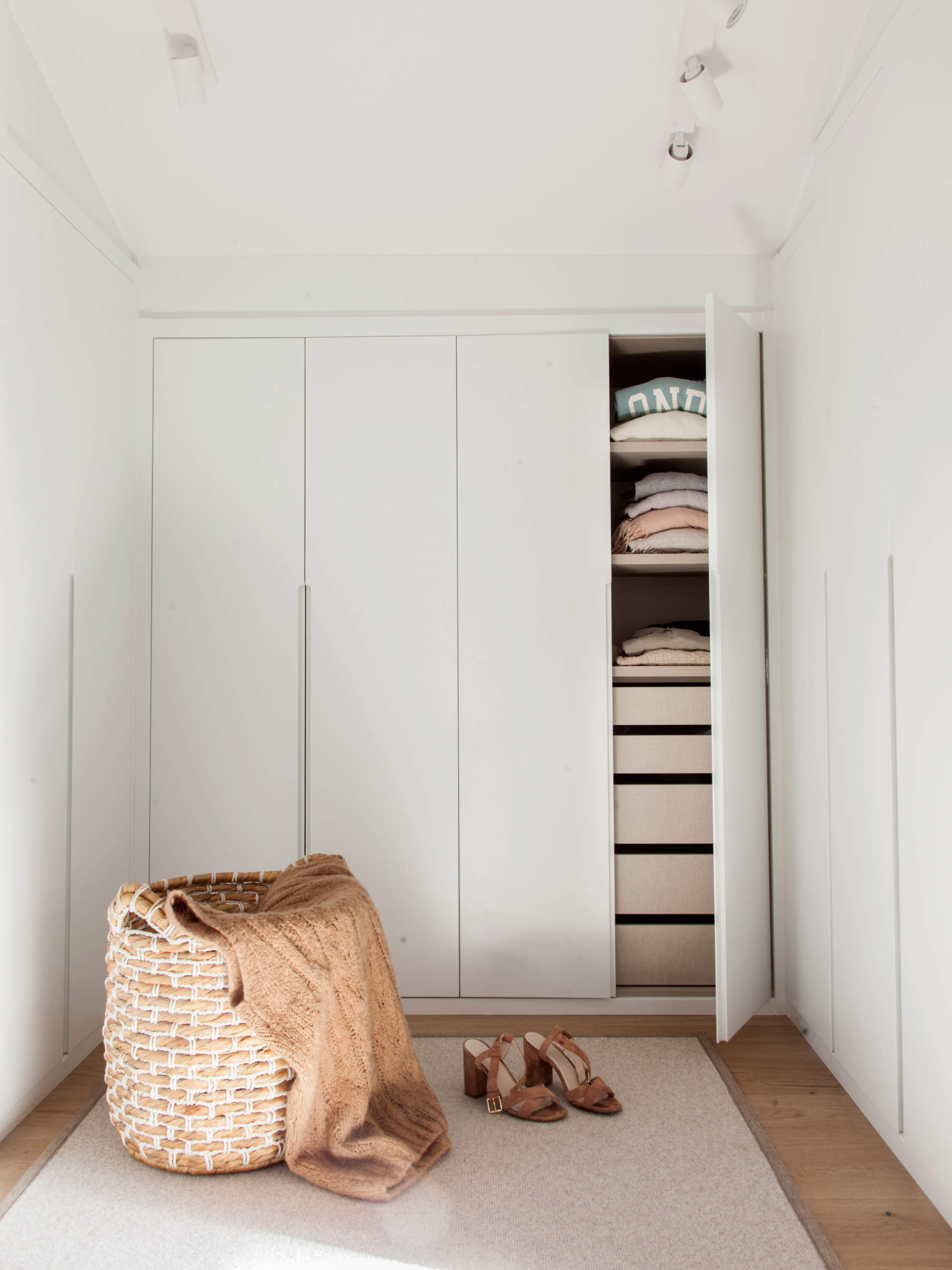 Vestidor con armarios lacados en blanco, alfombra y cesta