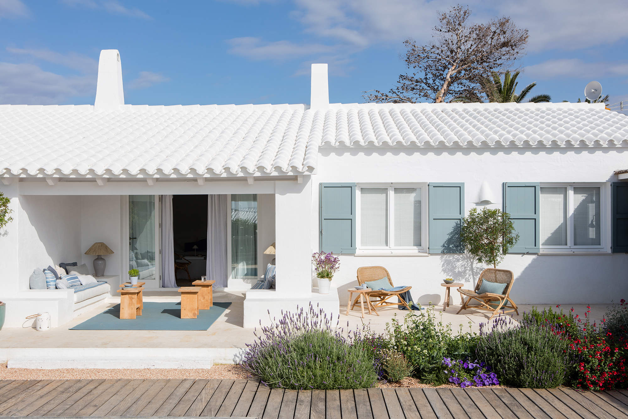 Porche mediterráneo con muebles blancos y alfombra azul, plantas aromáticas