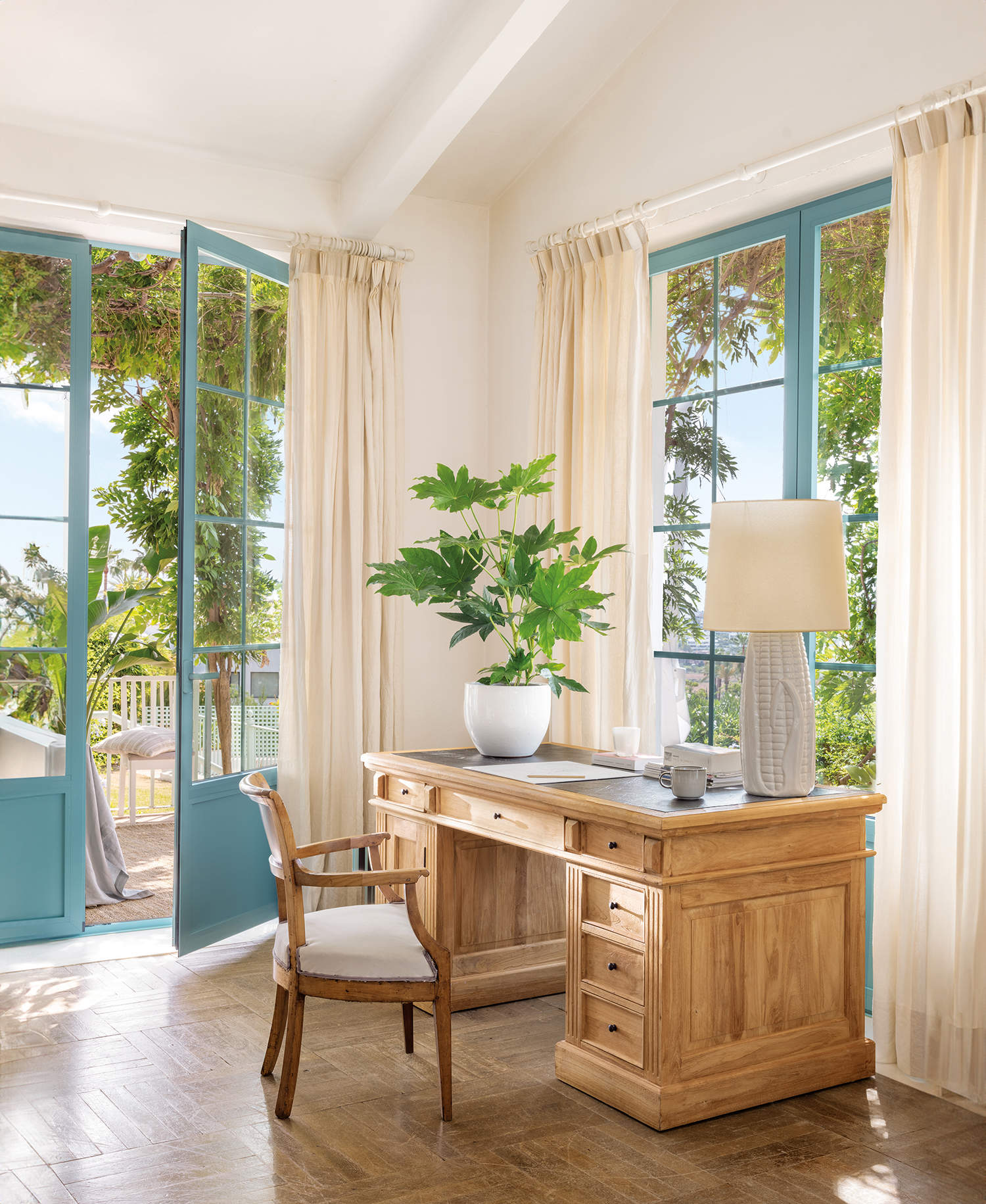 Salón con zona de escritorio de madera natural y ventanas con carpintería azul