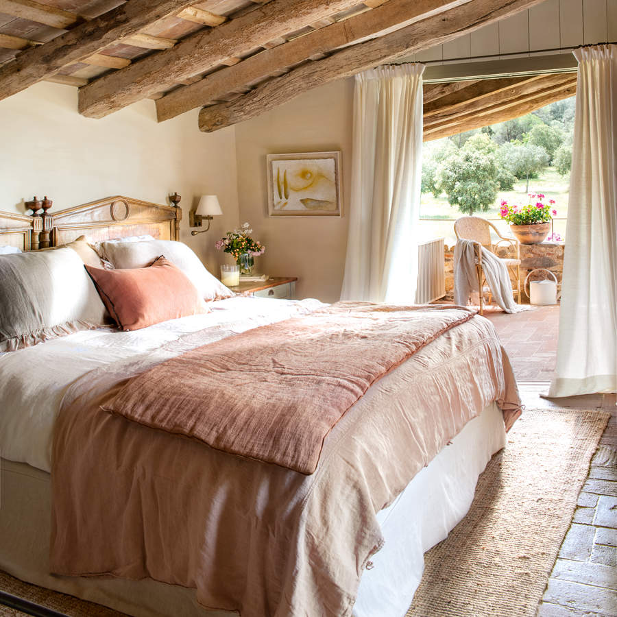 Dormitorio rústico con terraza, con vigas de madera, suelos de barro, alfombra de yute