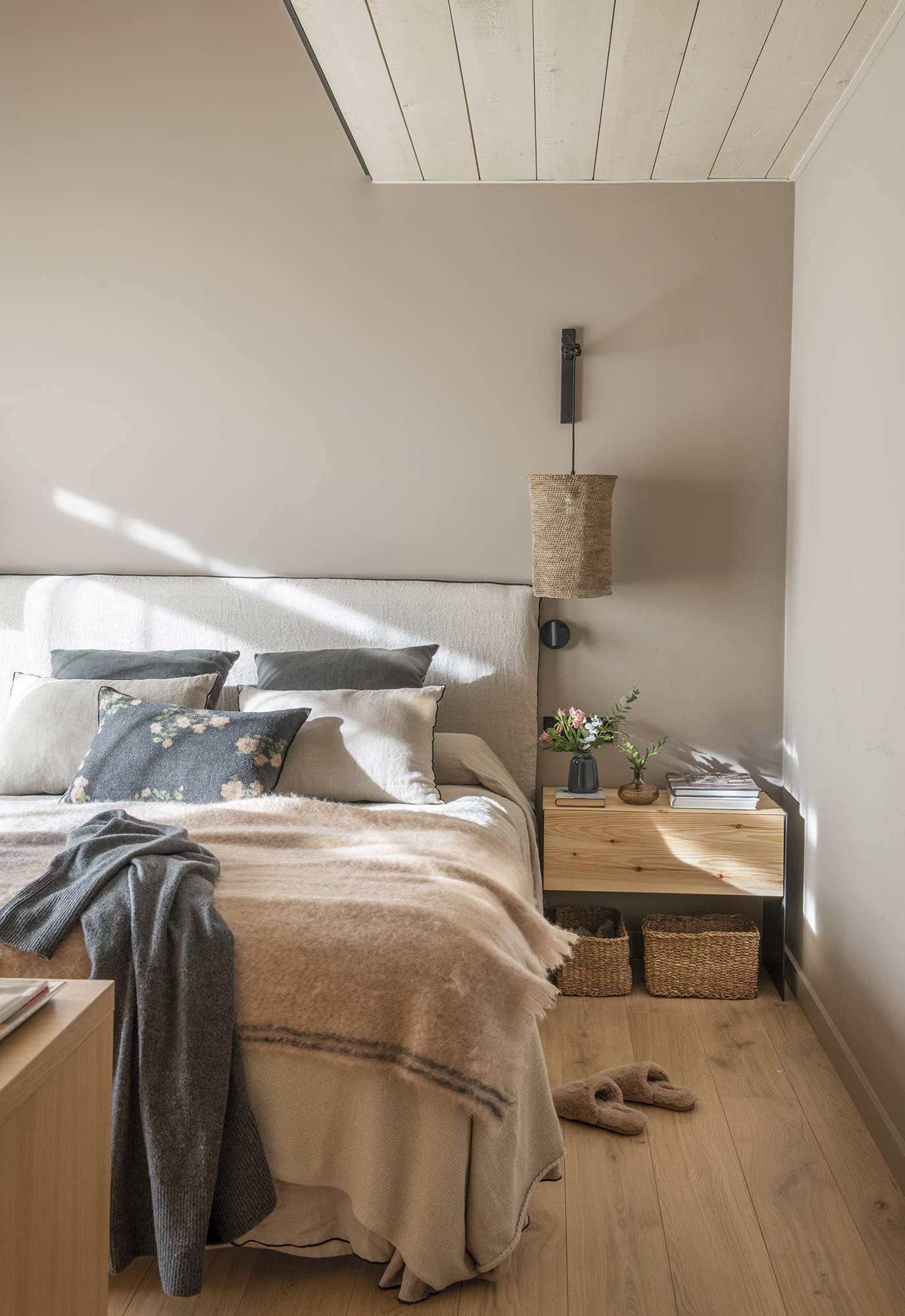 dormitorio principal con suelo de parquet, mesa de noche de madera, aplique de pared de fibra, cojín gris a flores, pintura de pared gris