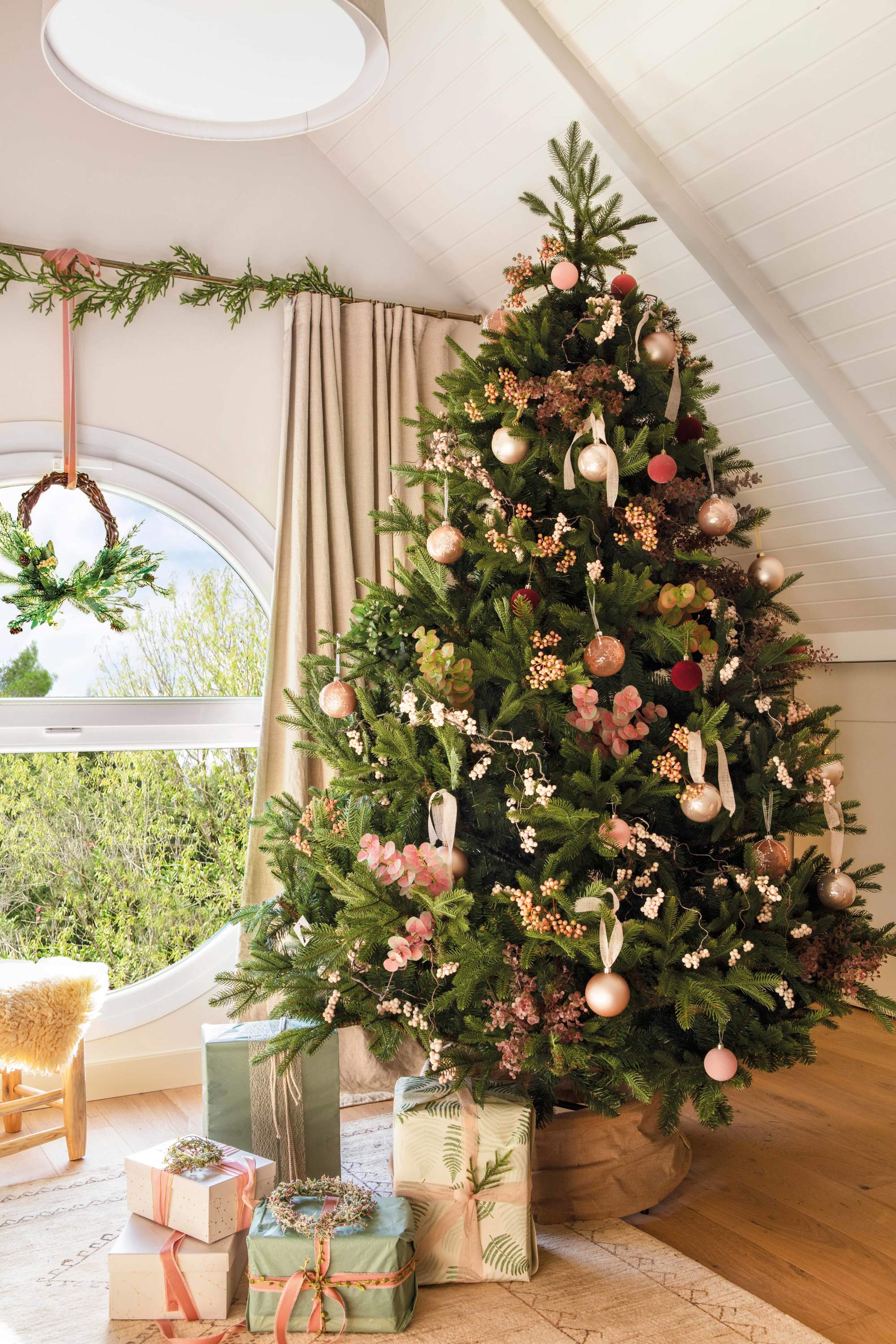 Salón decorado con árbol de Navidad en tonos pasteles, guirnalda en la ventana y regalos.