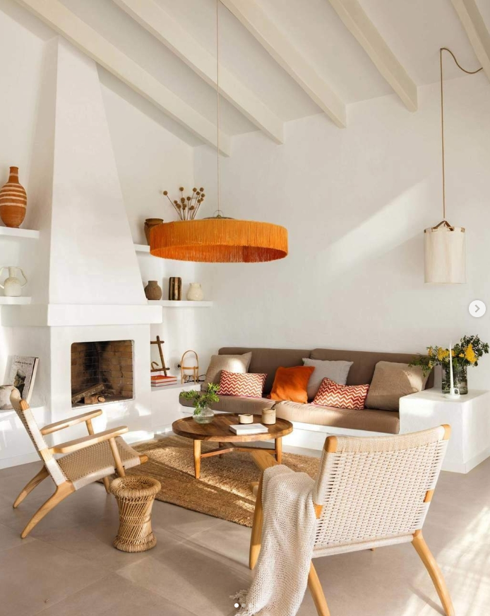 Salón blanco con muebles de obra, y muebles auxiliares en fibras naturales, naranjas y marrones.