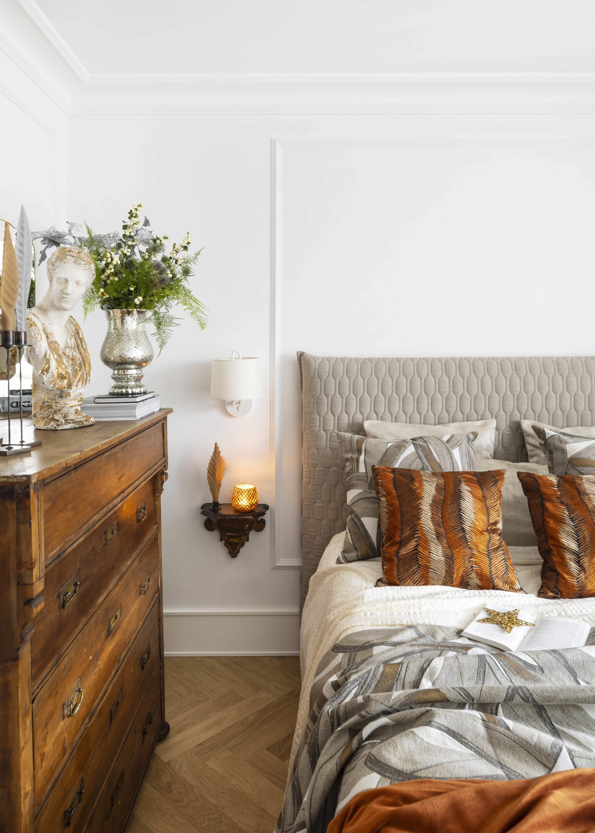 Dormitorio con cómoda de madera y textiles en terracota, grises, plateados y dorados