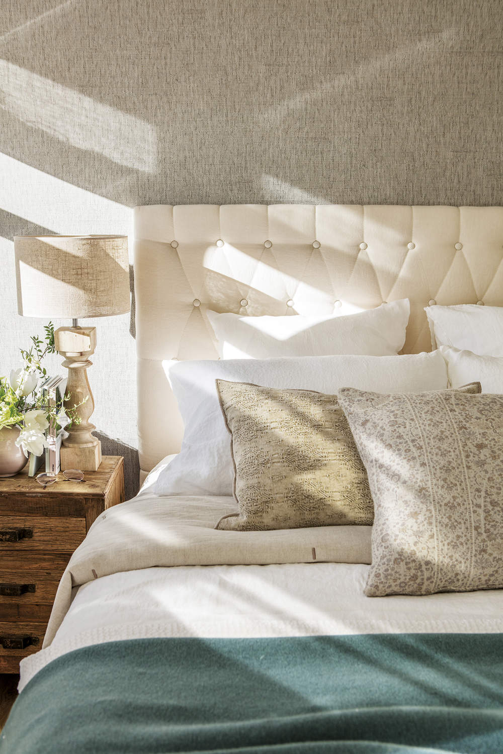 dormitorio principal con pared empapelada, suelo de madera y alfombra beige, cabecero tapizado de capitoné color marfil, ropa de cama blanca, mesita de noche con lámpara de mesa