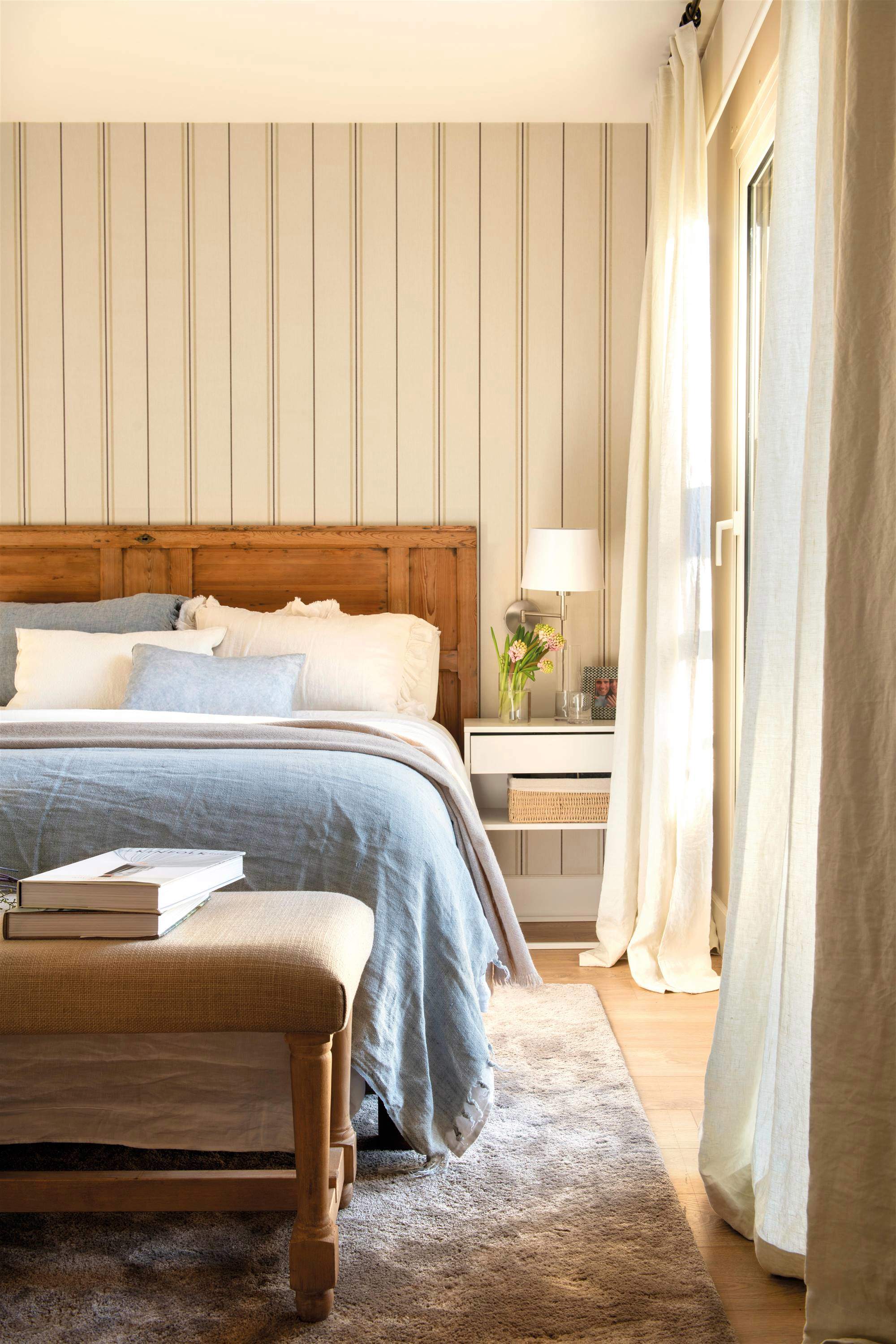 Dormitorio con cabecero de madera y papel pintado de rayas.