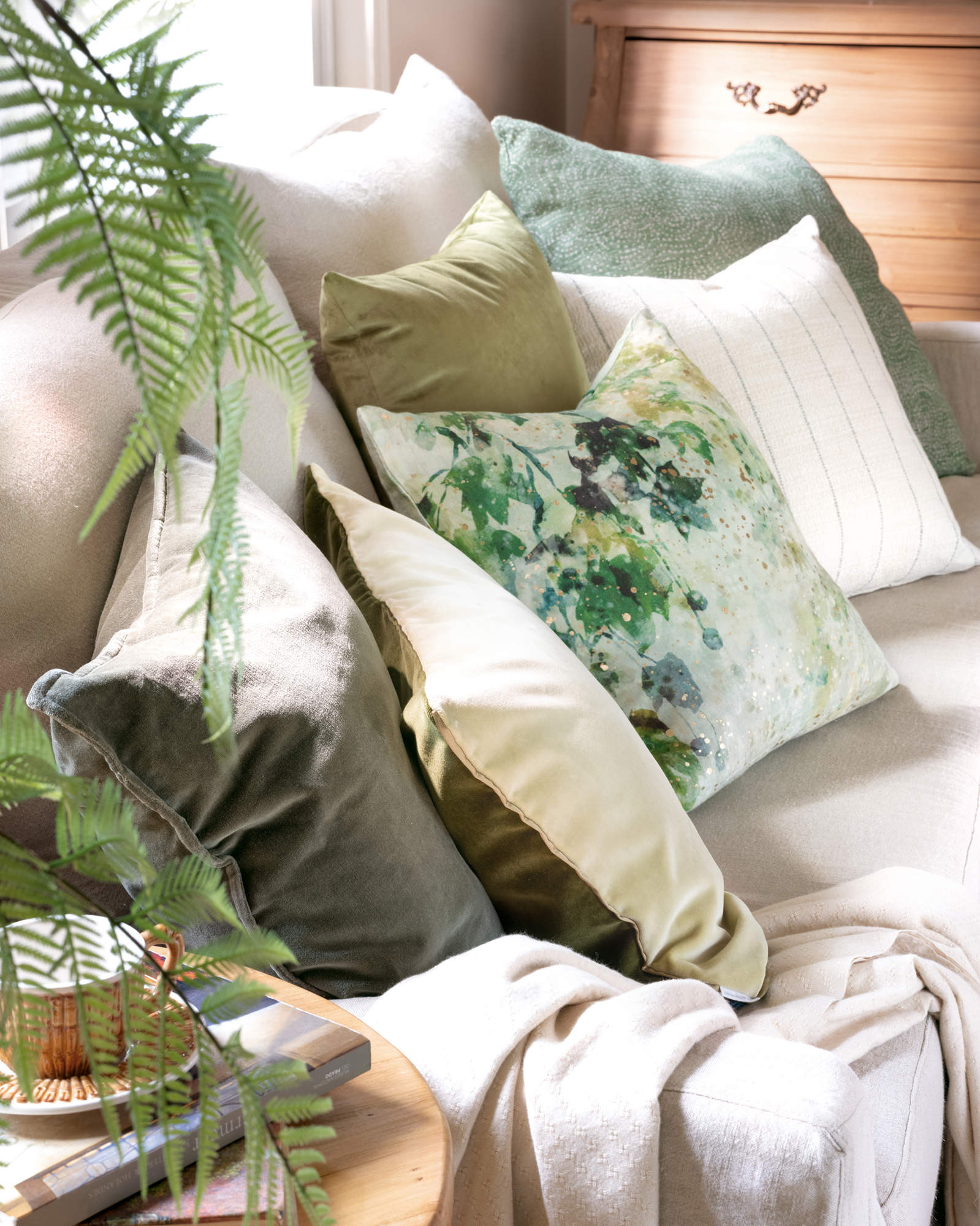 Detalle de cojines verdes y beige sobre sofá de lino.