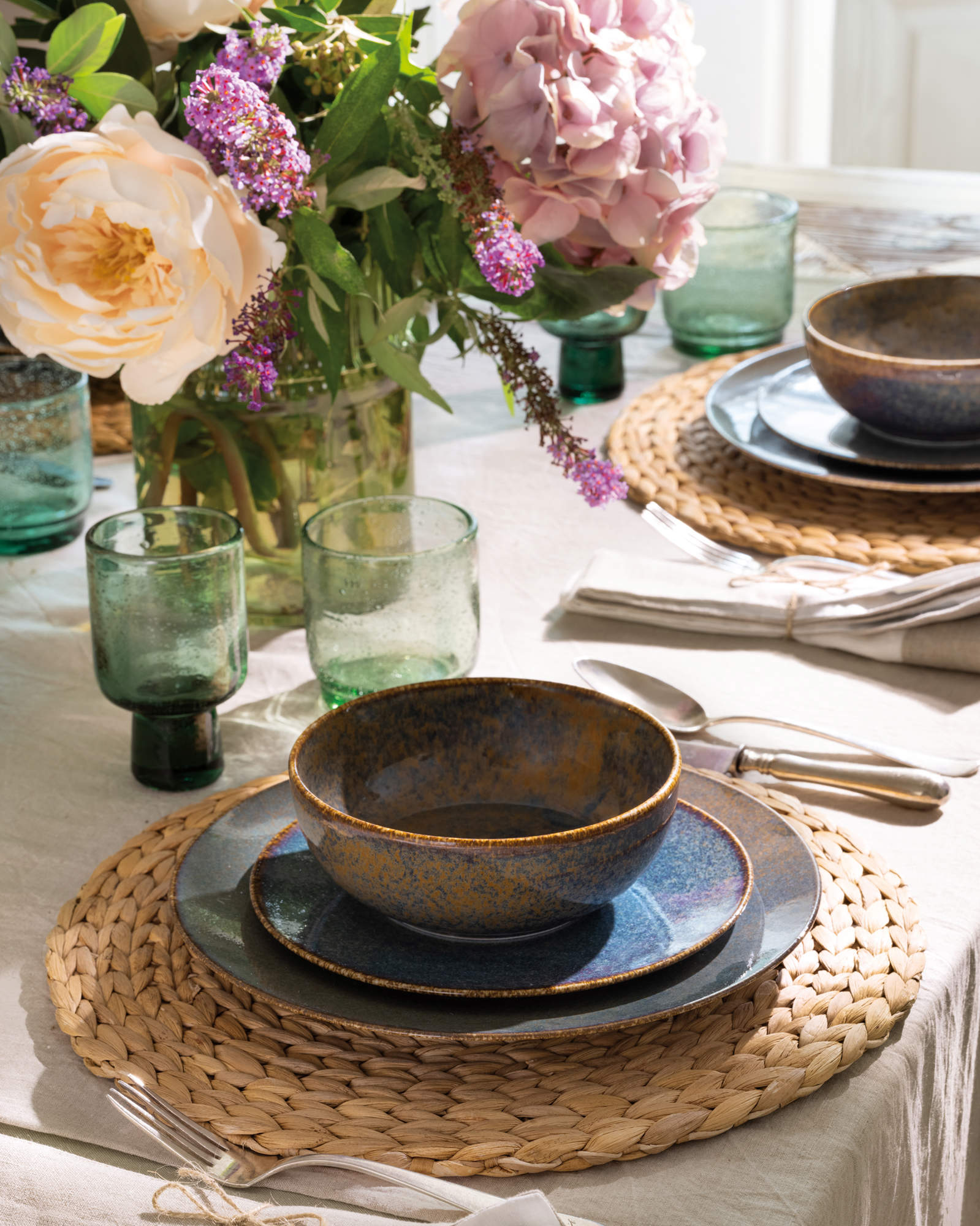 Detalle de la mesa con individuales de mimbre, arreglos florales y vajilla de estilo rústico.