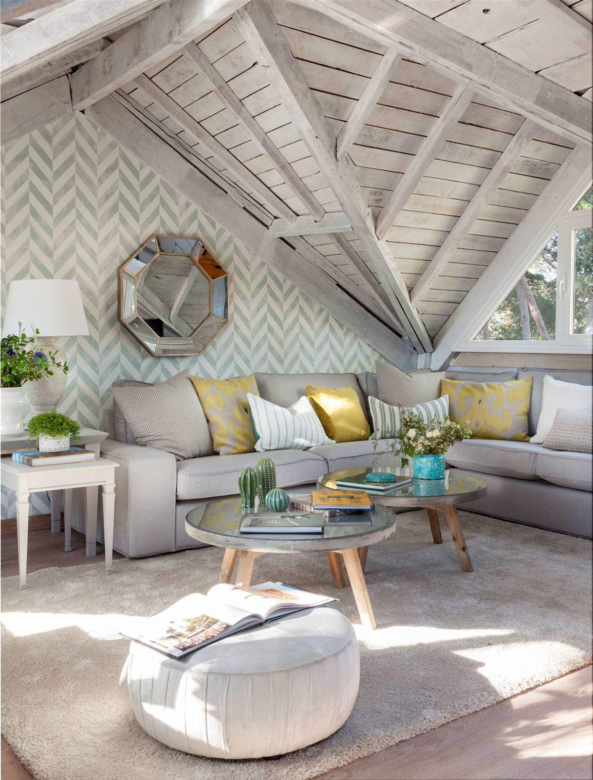 Salón abuhardillado con papel pintado geométrico tras el sofá y vigas grises