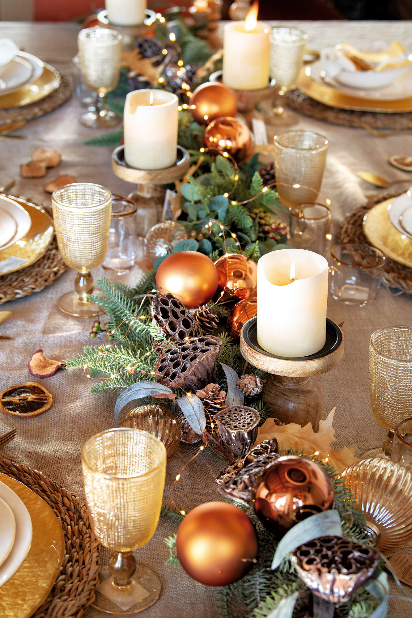 Centro de mesa con guirnalda de abeto, bolas naranjas, y candelabros de madera.