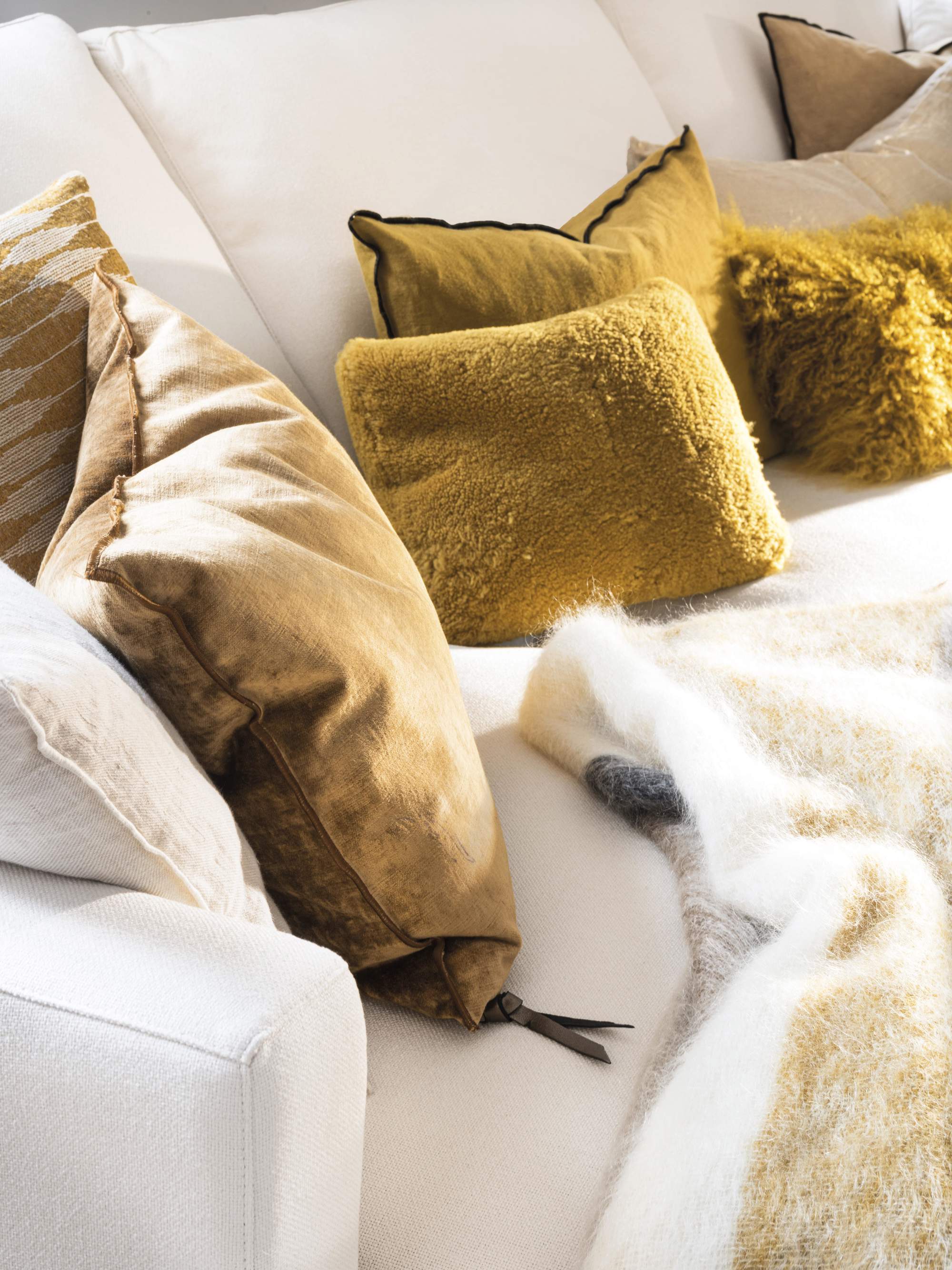 Detalle de cojines mostaza, beige y blanco sobre sofá blanco.
