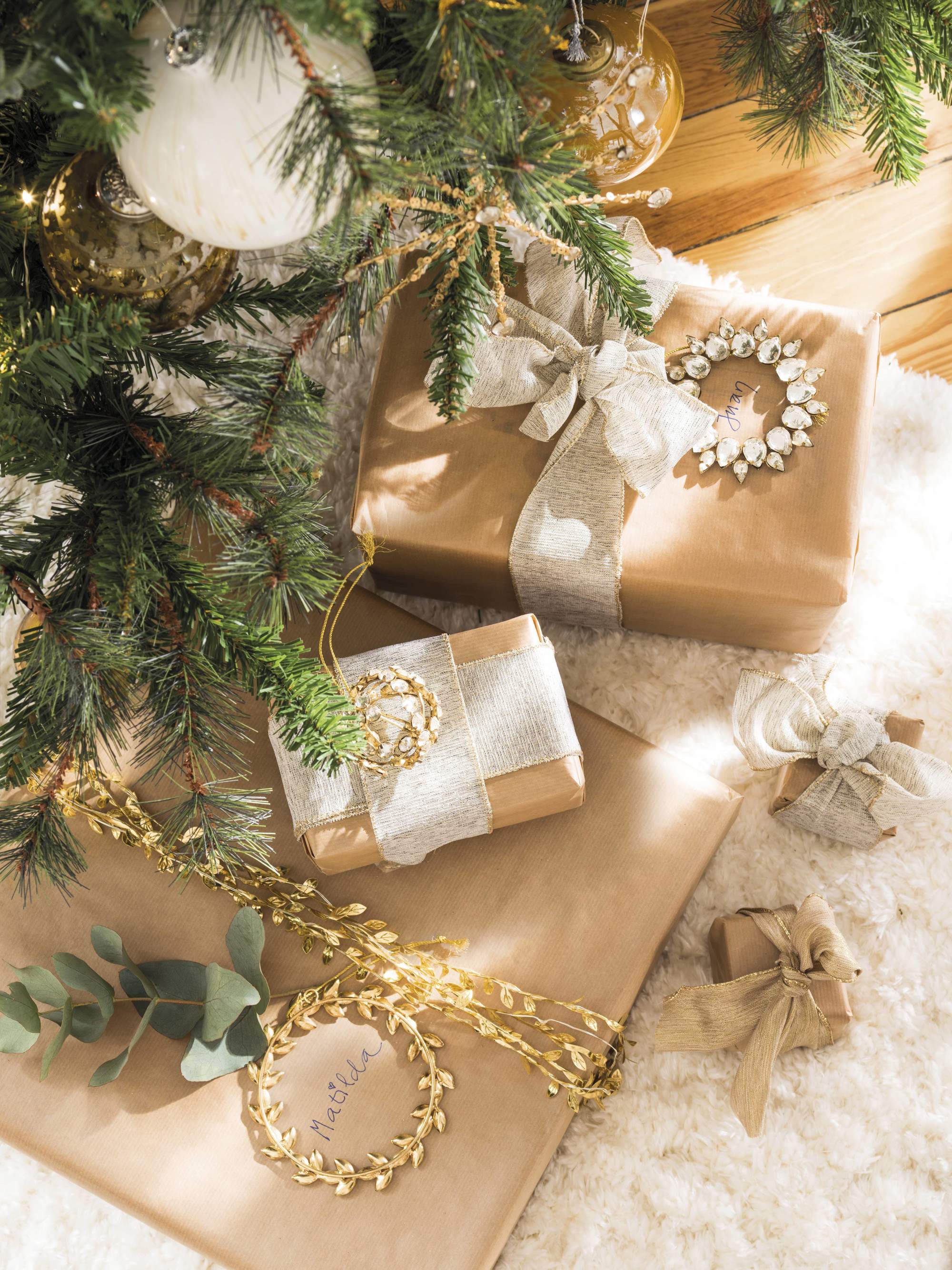 Regalos empaquetados en dorado y plata bajo el árbol de Navidad.