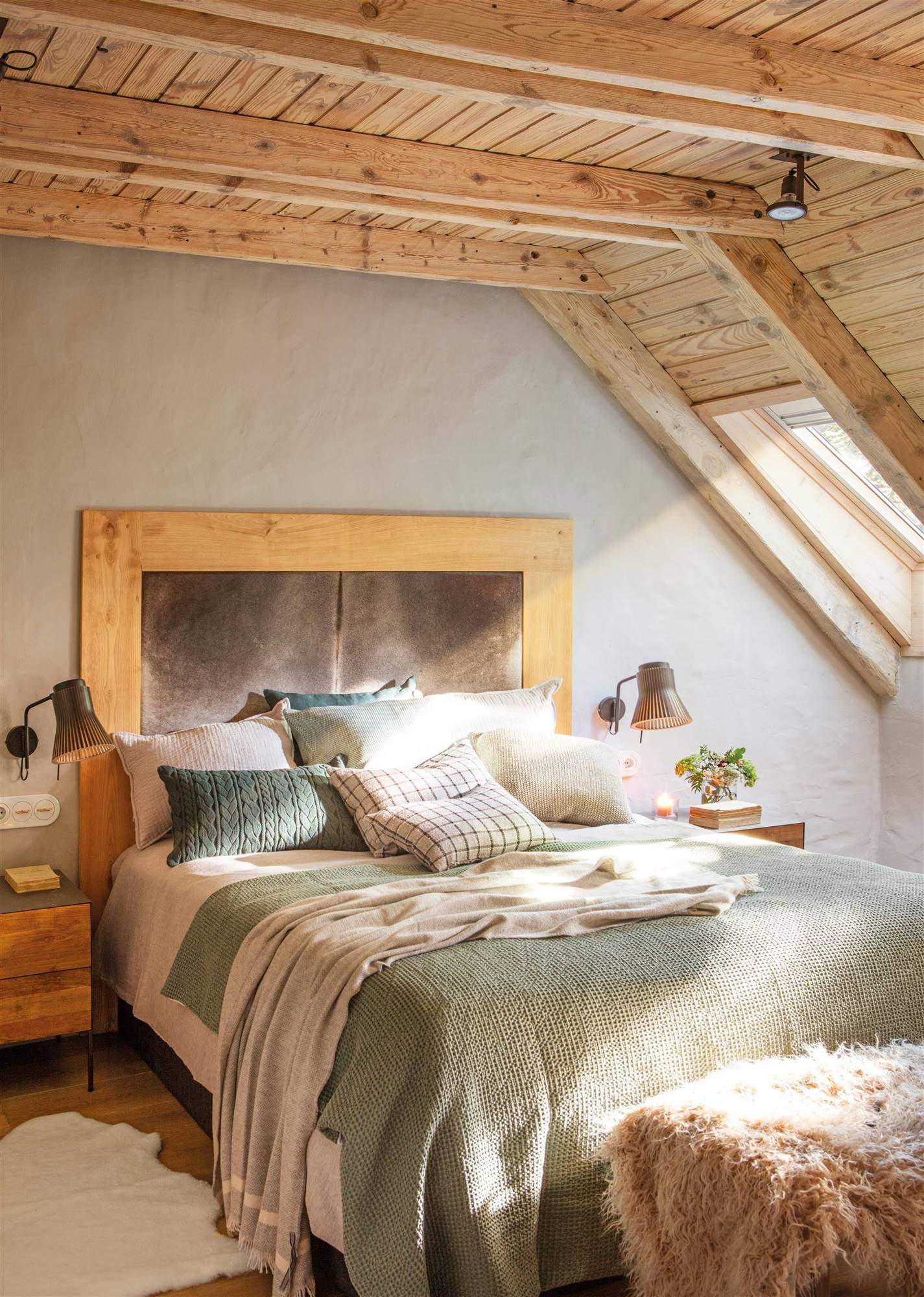 Dormitorio con techo de madera abuhardillado, cabecero de cuero y cojines verdes