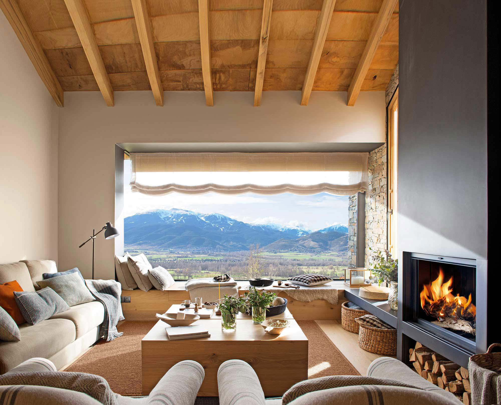 Salón de montaña con chimenea, ventanal y mesa de madera maciza