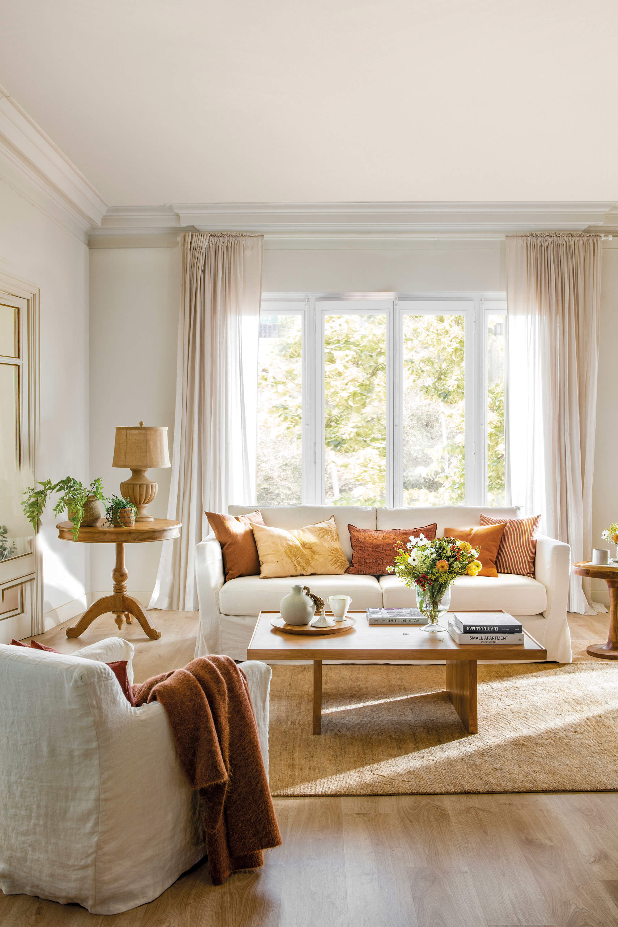 Salón con sofás blancos, cojines en colores cálidos y muebles de madera.