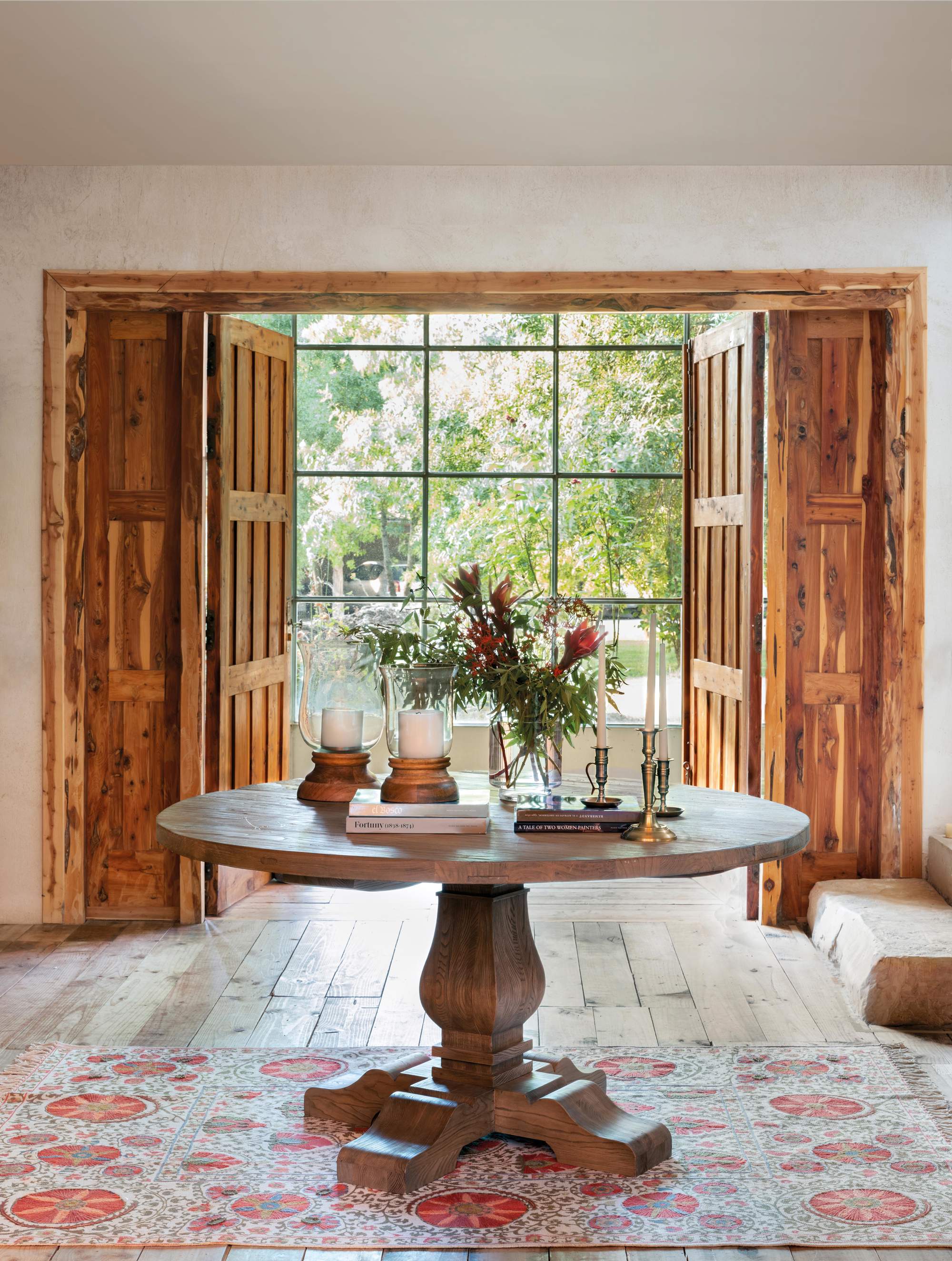 Recibidor con mesa redonda de madera en el centro, alfombra estampada y contraventanas de madera