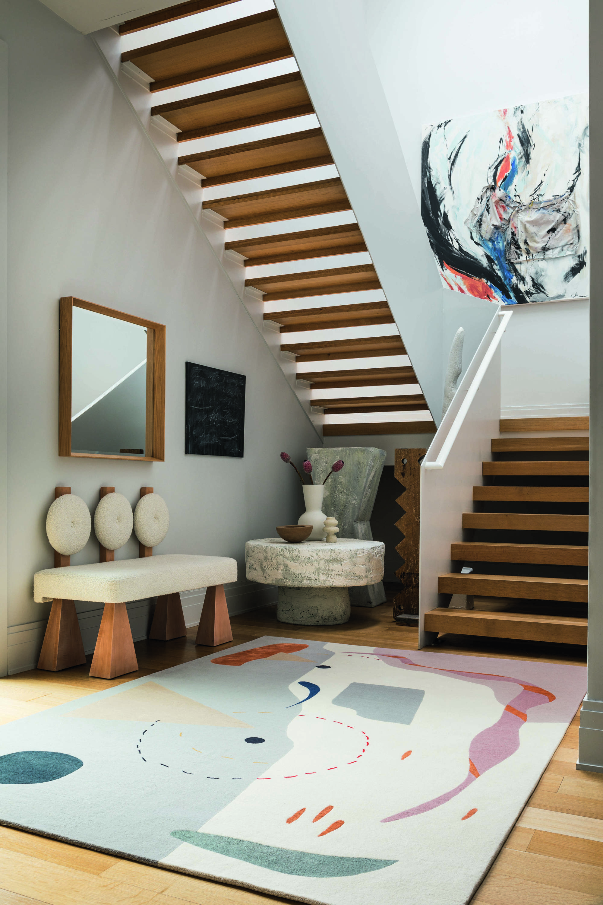 Recibidor con escalera de madera, banco, espejo y alfombra