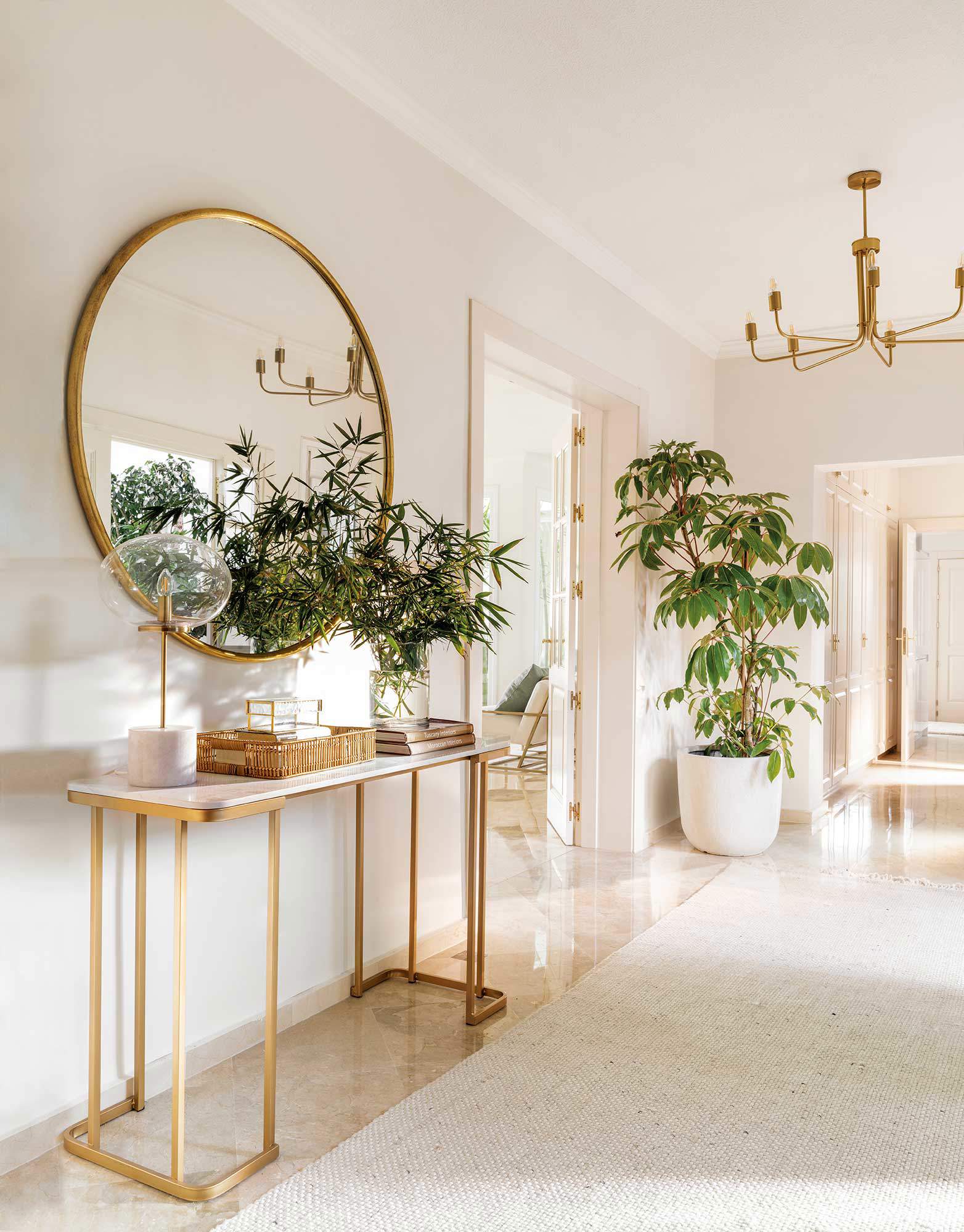 Recibidor blanco con muebles dorados y plantas. 