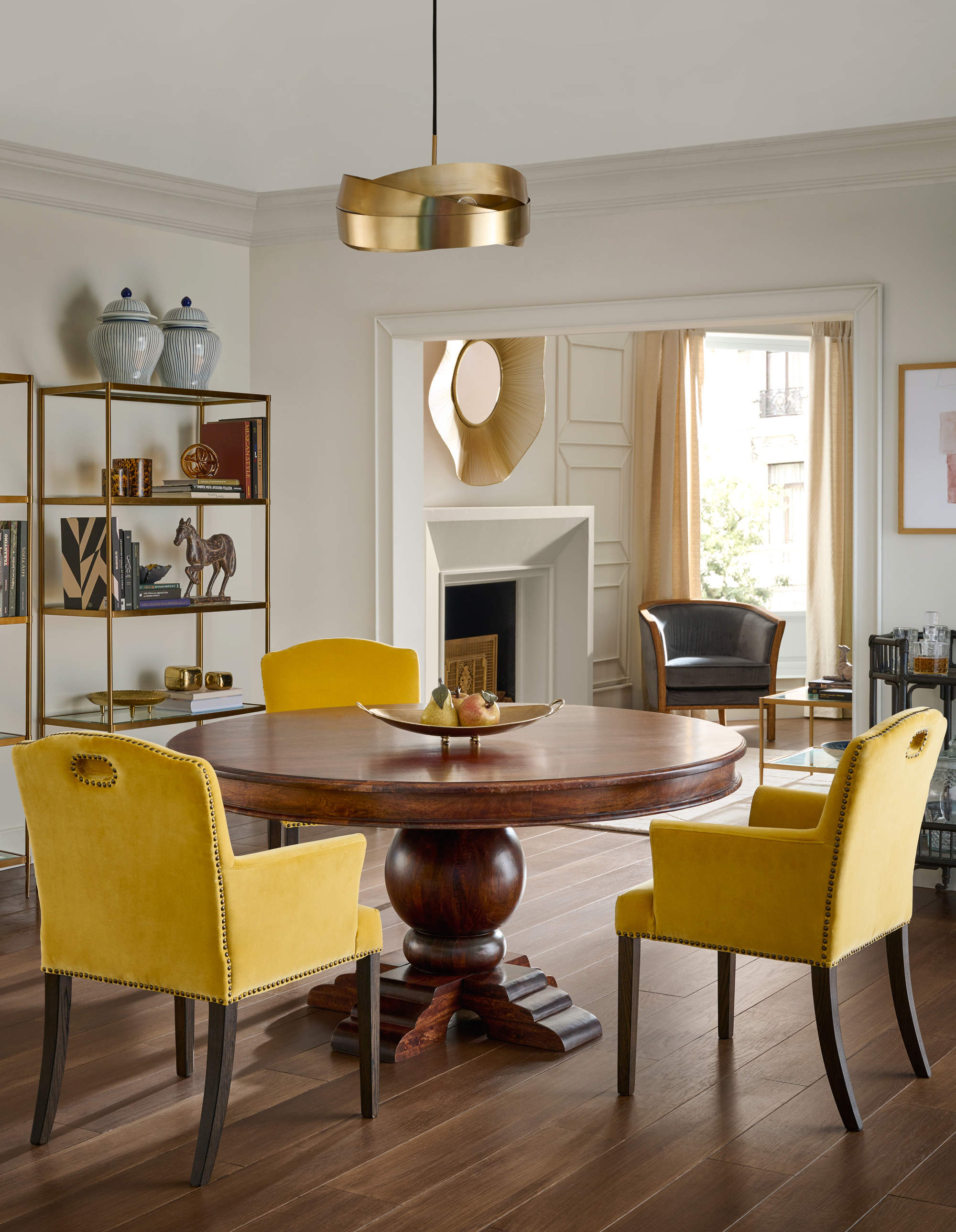 Comedor con mesa redonda de madera, sillas tapizadas en mostaza y lámpara de techo en dorado.