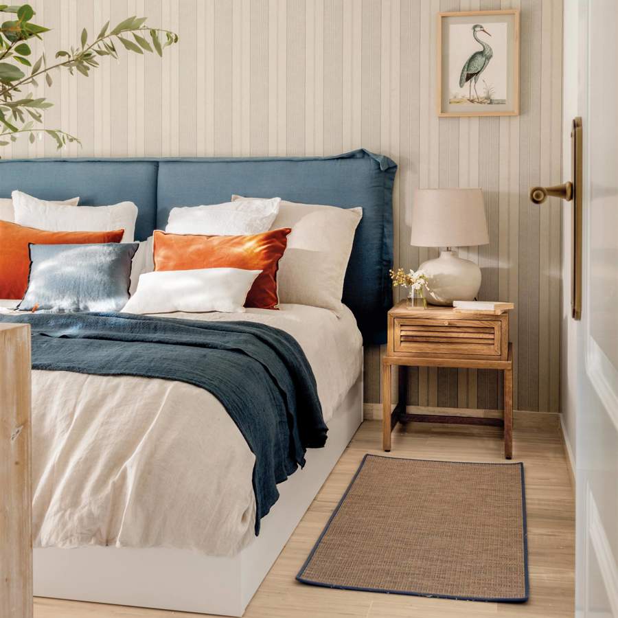 Dormitorio con cabecero tapizado en azul y papel pintado de rayas