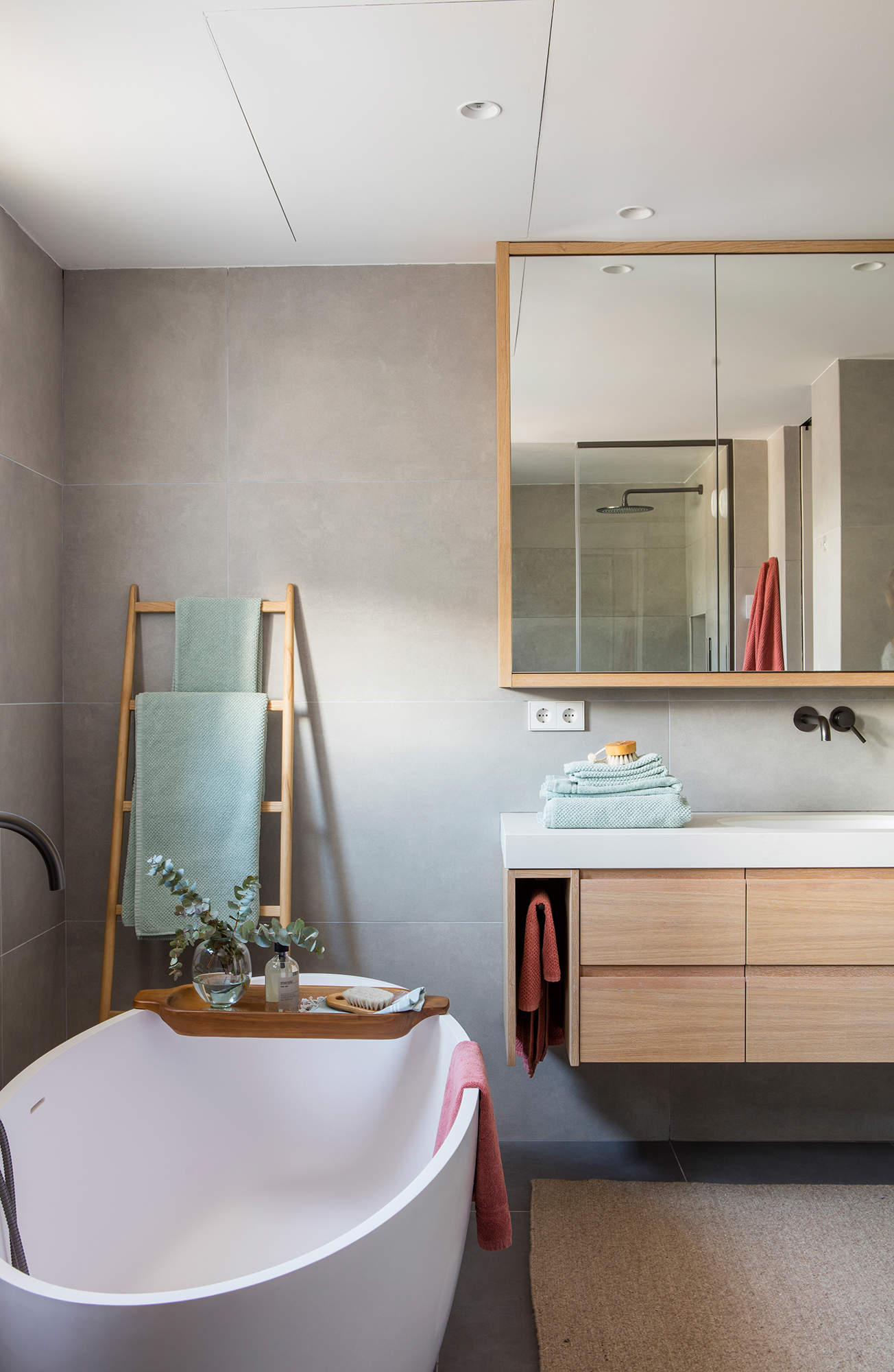 Cuarto de baño gris con muebles y complementos de madera clara.