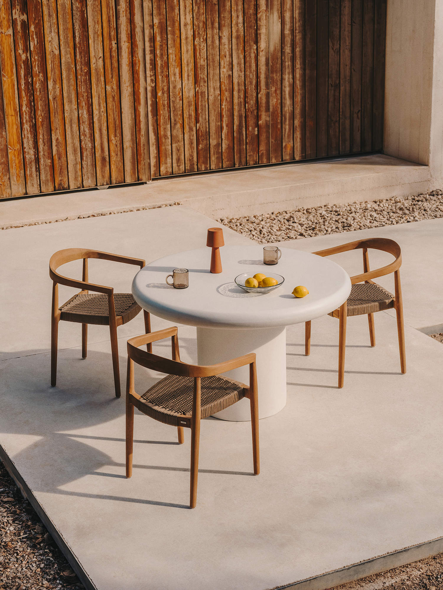 Comedor de exterior con mesa blanca y sillas de madera y cuerda.