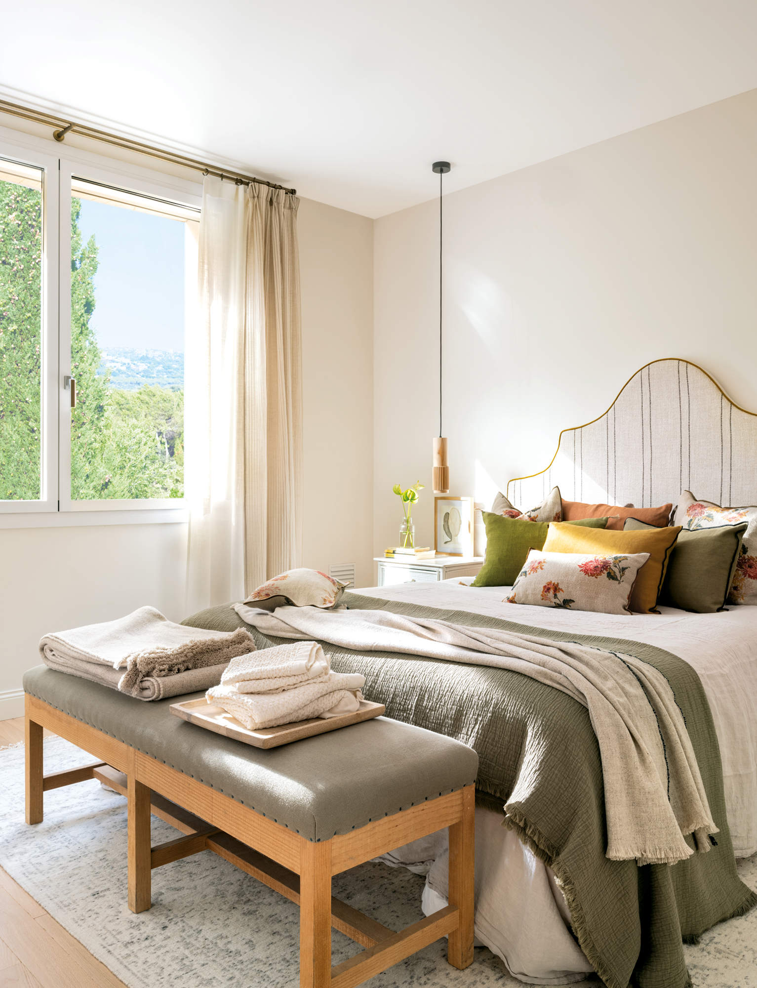 Dormitorio luminoso con ropa de cama verde y cabezal tapizado a rayas.