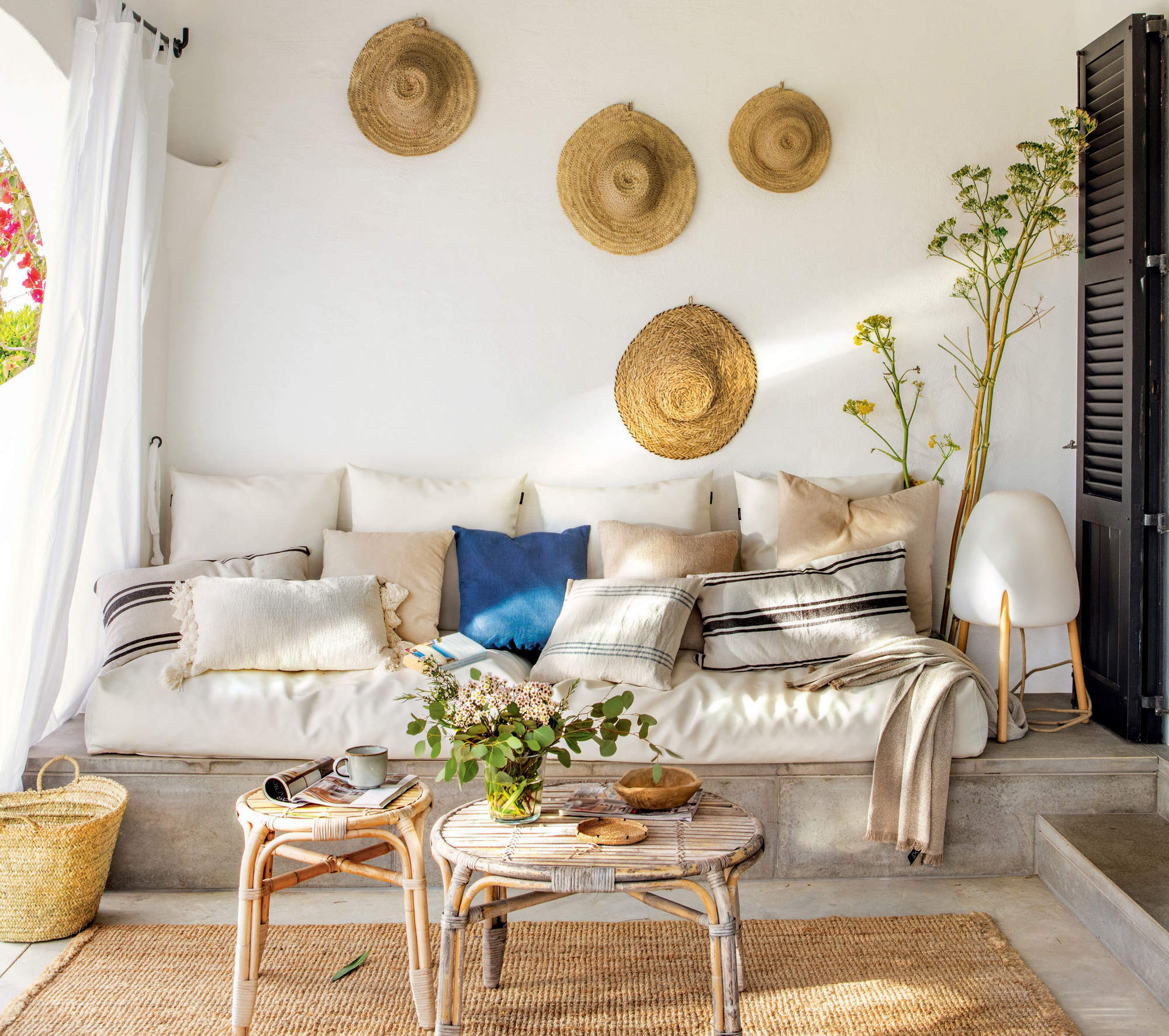 Salón de veranocon sofá de obra, mesas redondas y sombreros de paja decorando la pared
