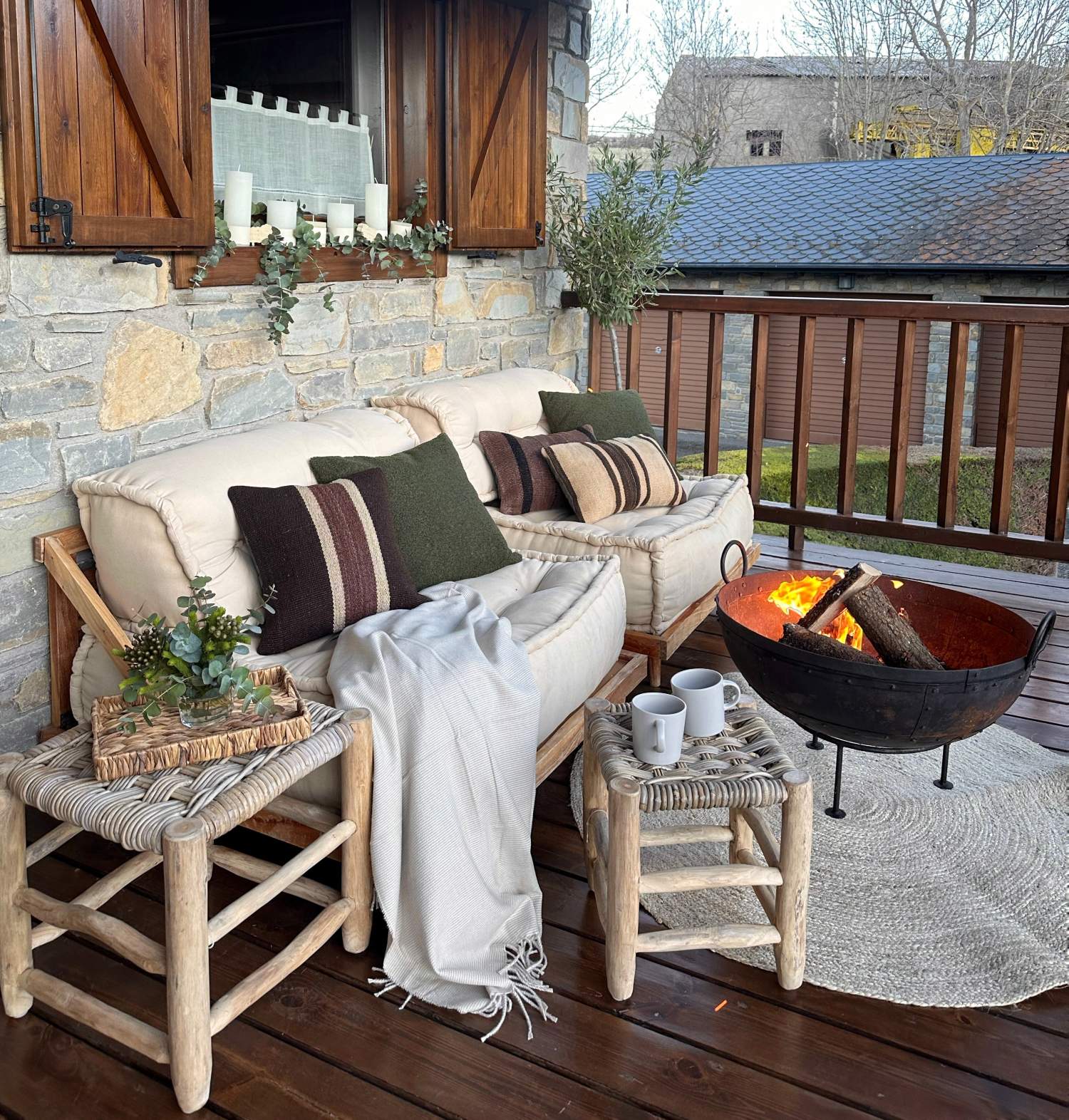 Terraza decorada con sofás en color crudo, chimenea portátil y muebles de madera.
