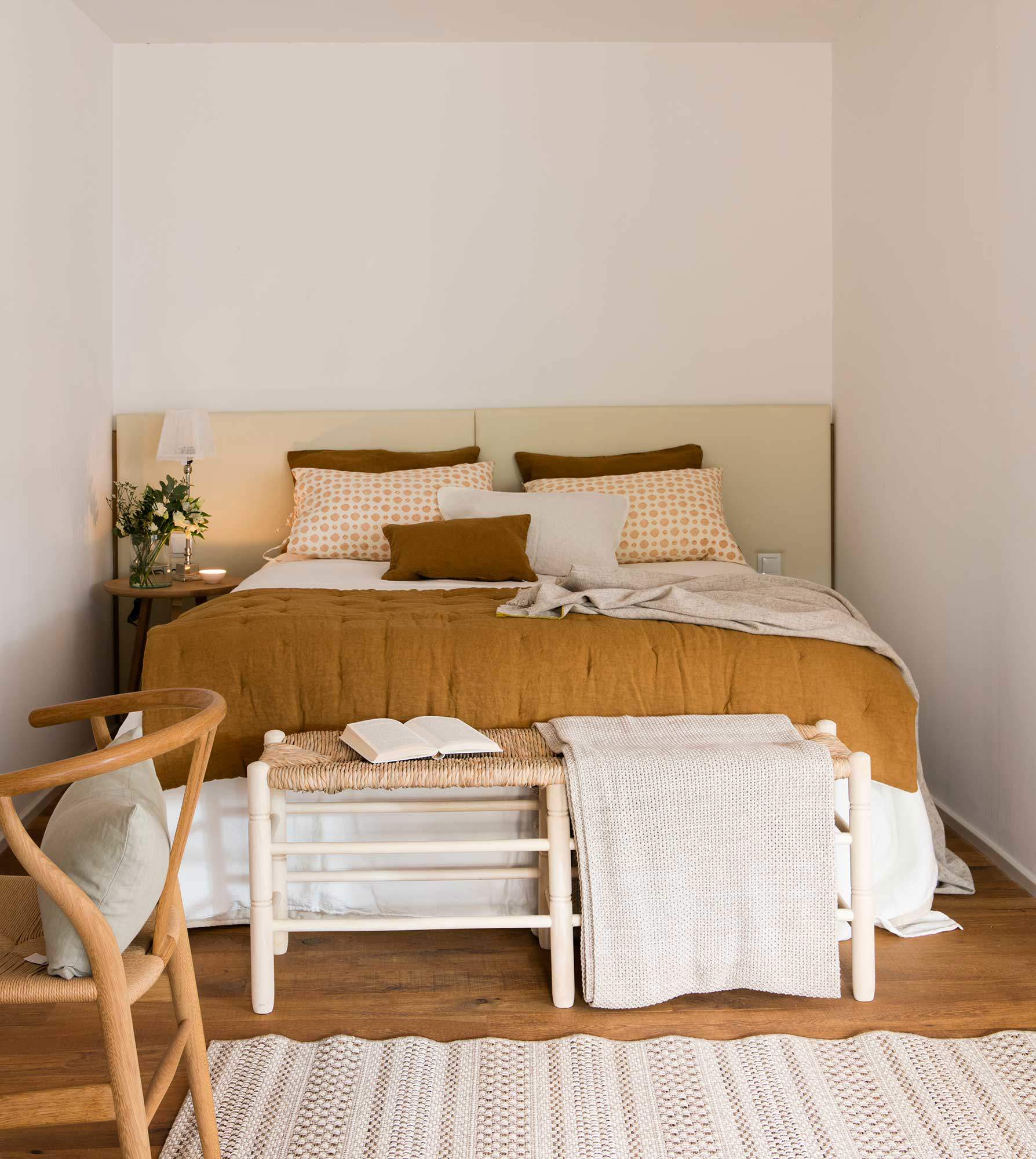 Dormitorio pequeño con cabecero a medida, mesita de noche redonda y banco a los pies de la cama