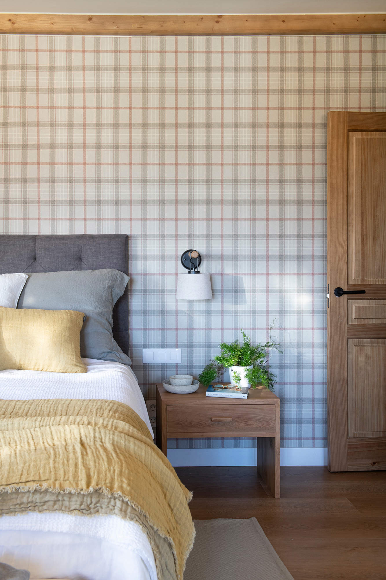 Dormitorio pequeño con papel de cuadros y mesita de noche de madera