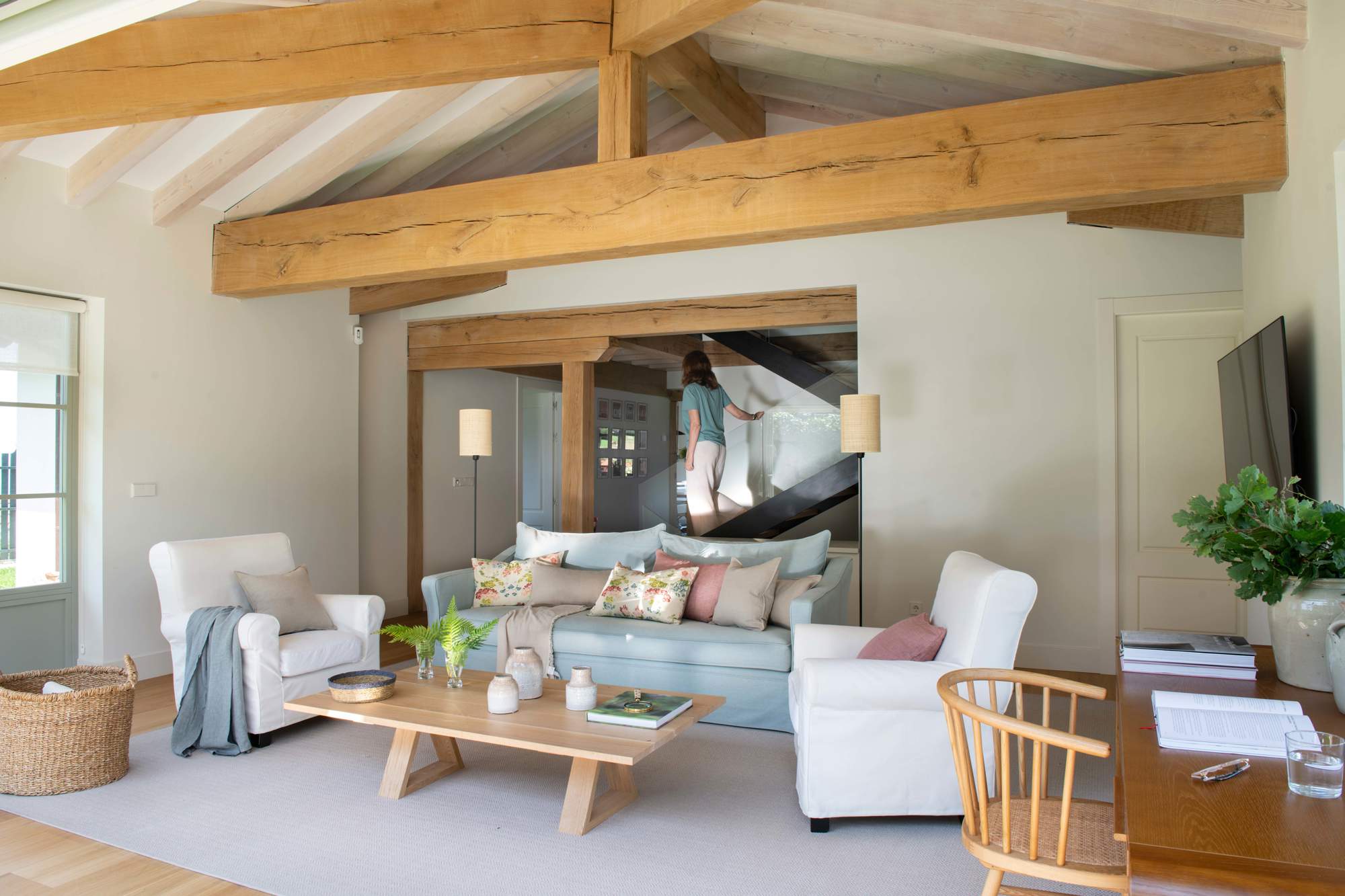 Salón con vigas en el techo, sofá azul, butacas blancas, mesa de madera y alfombra blanca