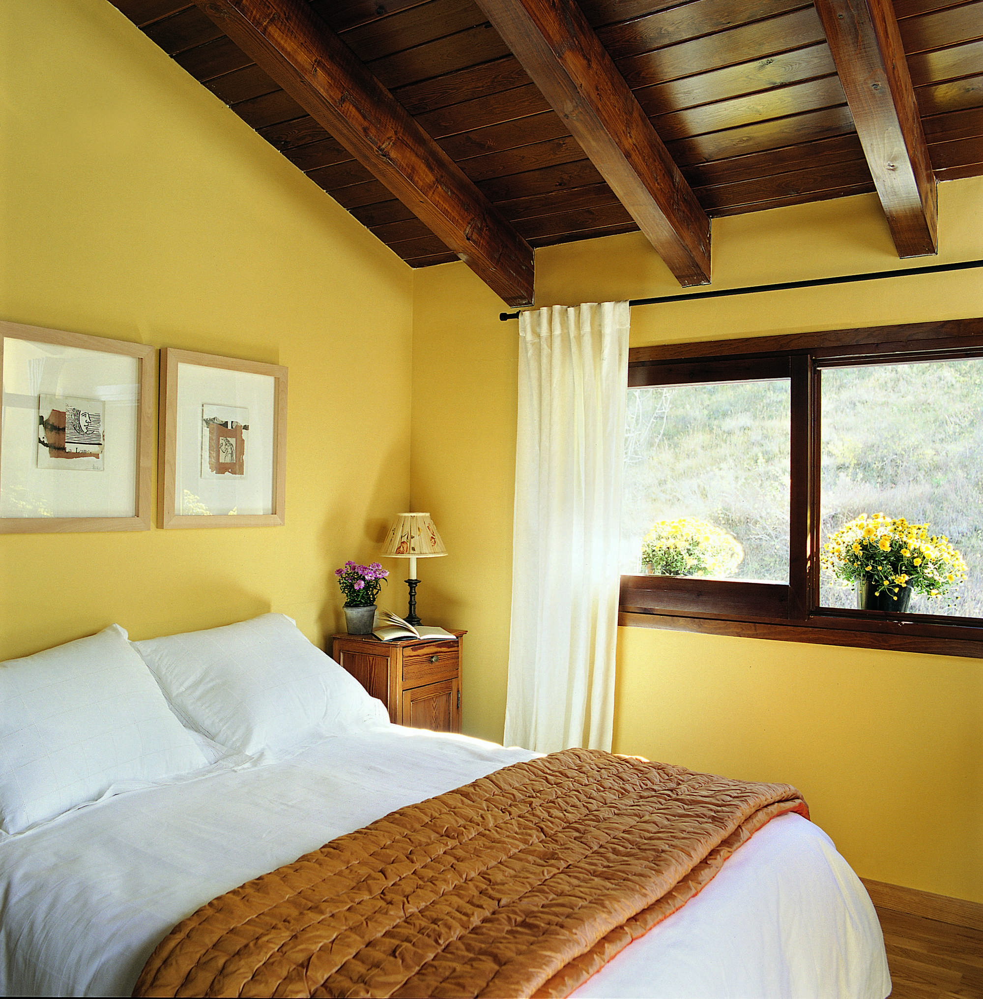 Dormitorio con paredes pintadas de amarillo, vigas de madera y cuadros