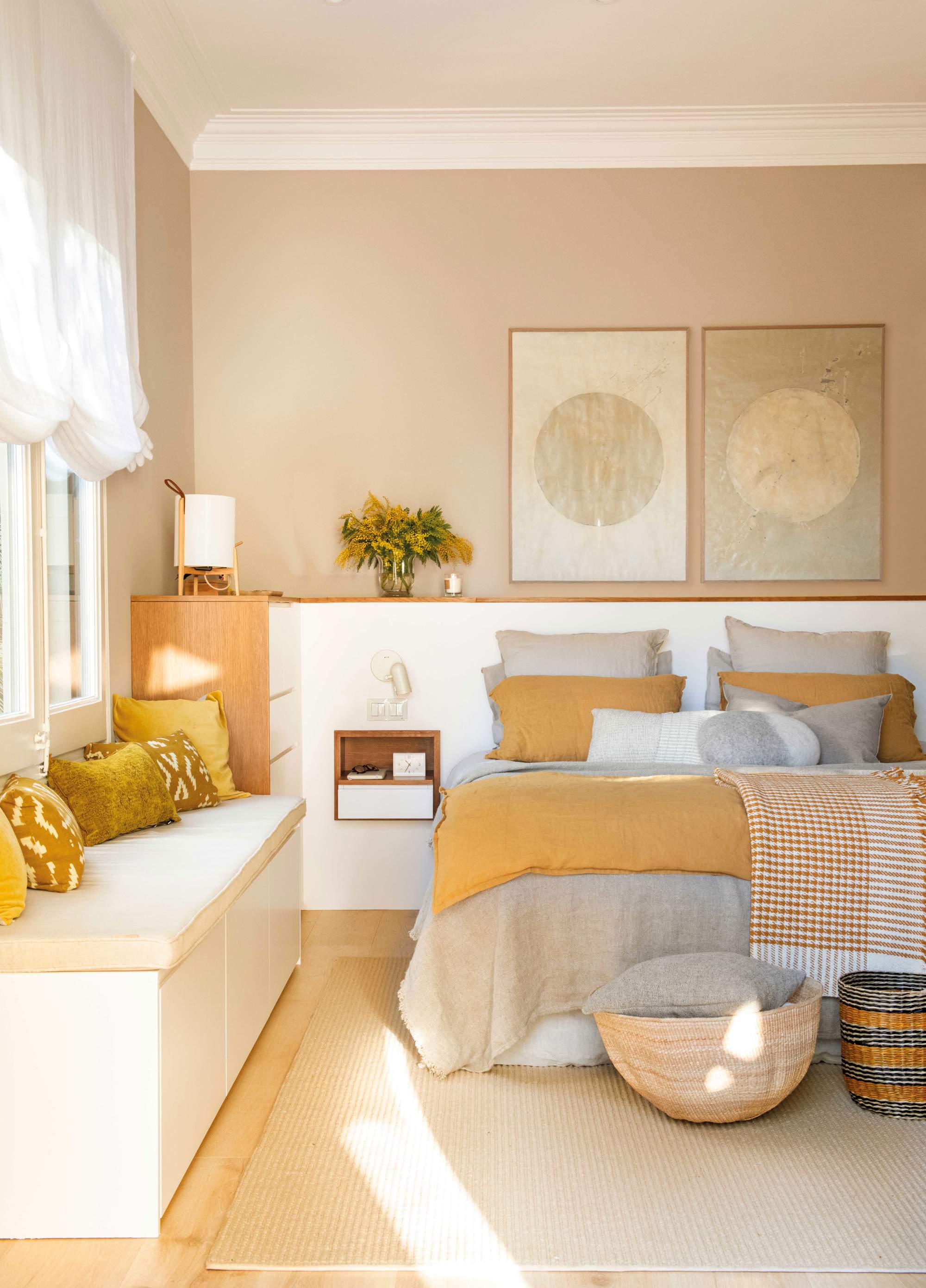 Dormitorio con paredes pintadas en beige, banco y ropa de cama en color mostaza y gris