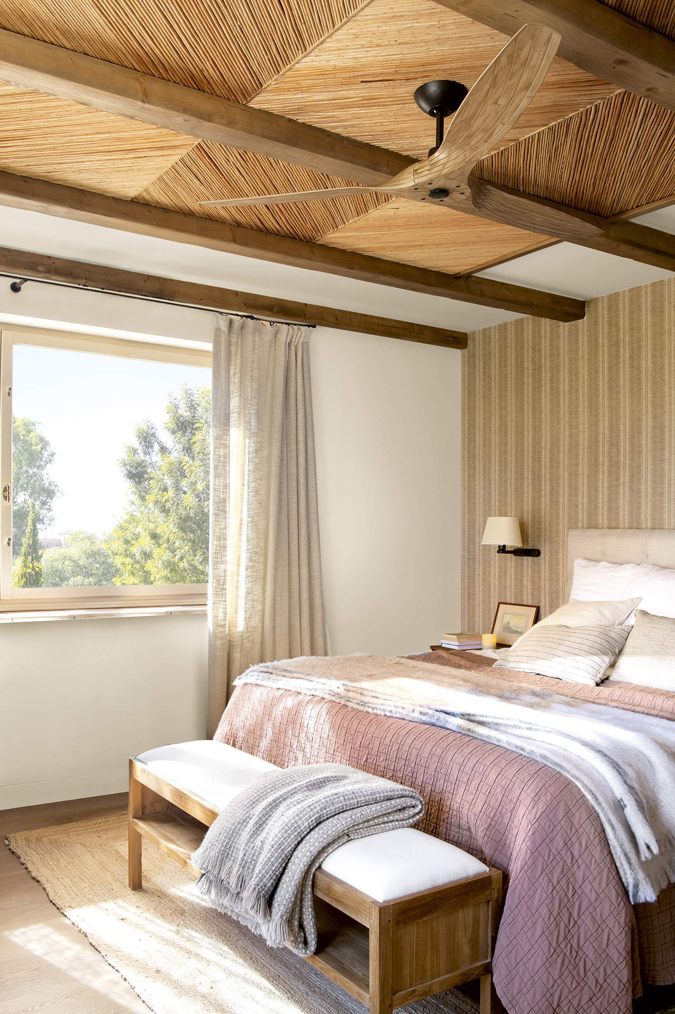 dormitorio con pared empapelada y techo de fibra, ropa de cama rosa y banqueta blanca