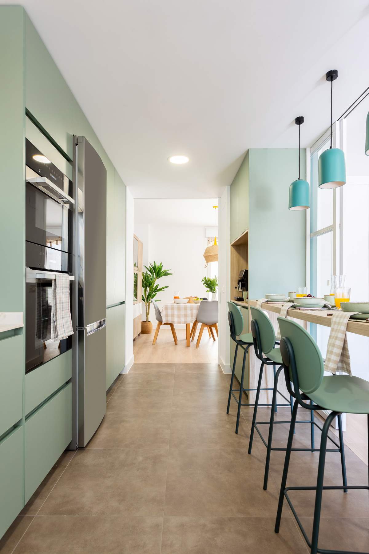 Una cocina larga y estrecha con desayunador, barra y mobiliario de color verde