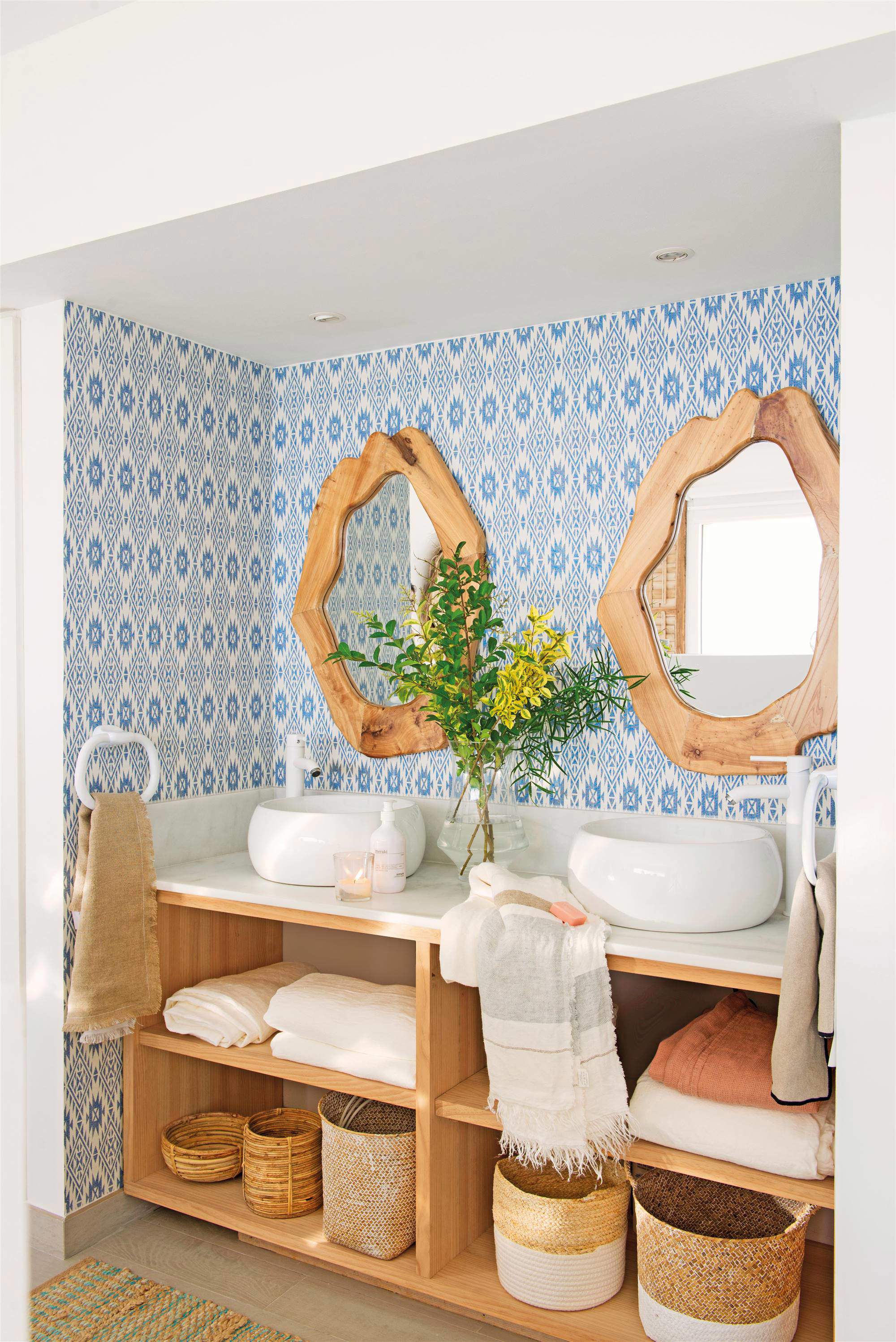 Baño con mueble abierto, papel pintado geométrico en azul y espejos de madera